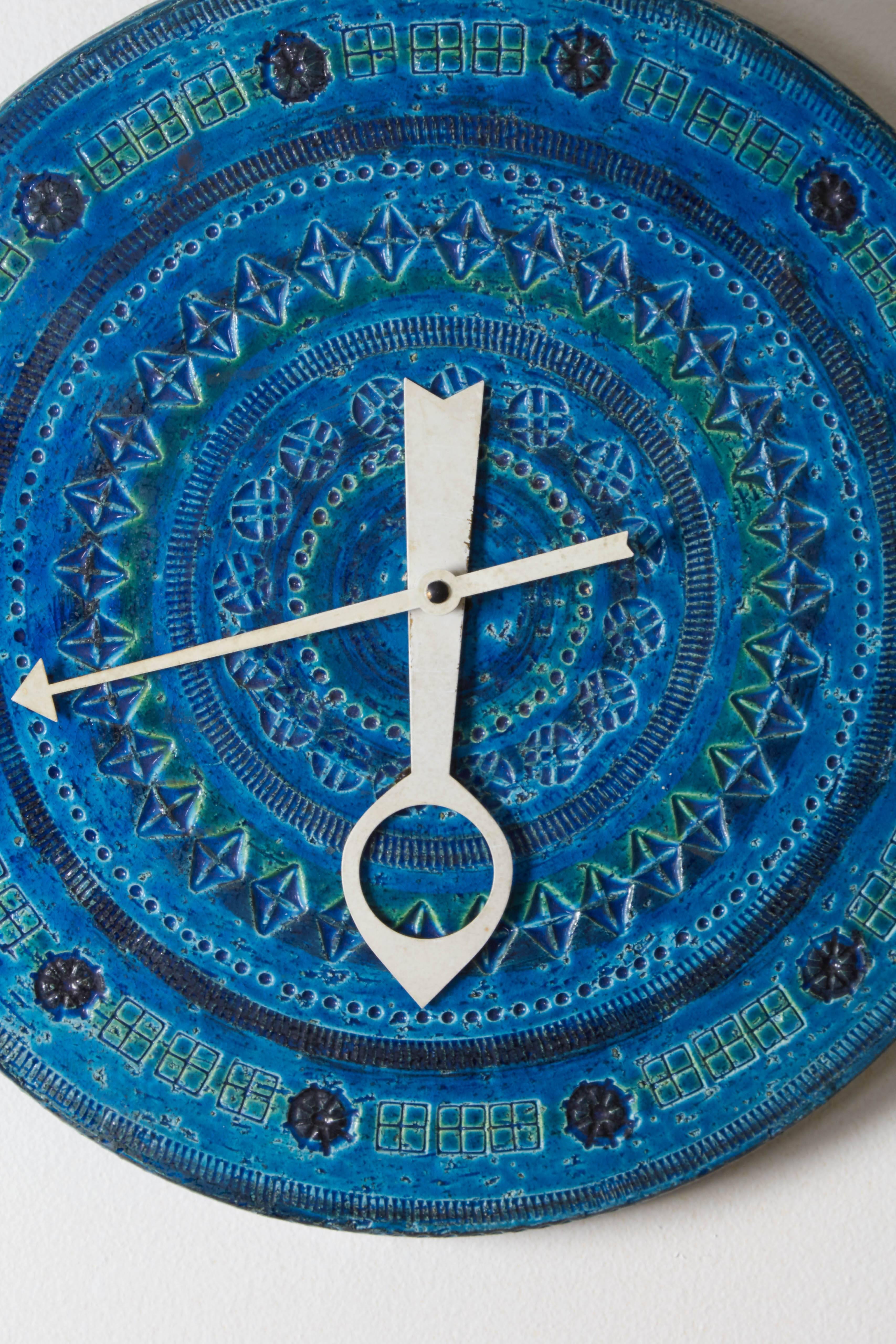 A ceramic wall clock by Bitossi, produced in Italy, circa 1960s for Meridian Clocks, imported by Raymor, the face intricately incised and glazed in Rimini Blu, with metal hour and minute hands. This clock is in very good vintage condition,
