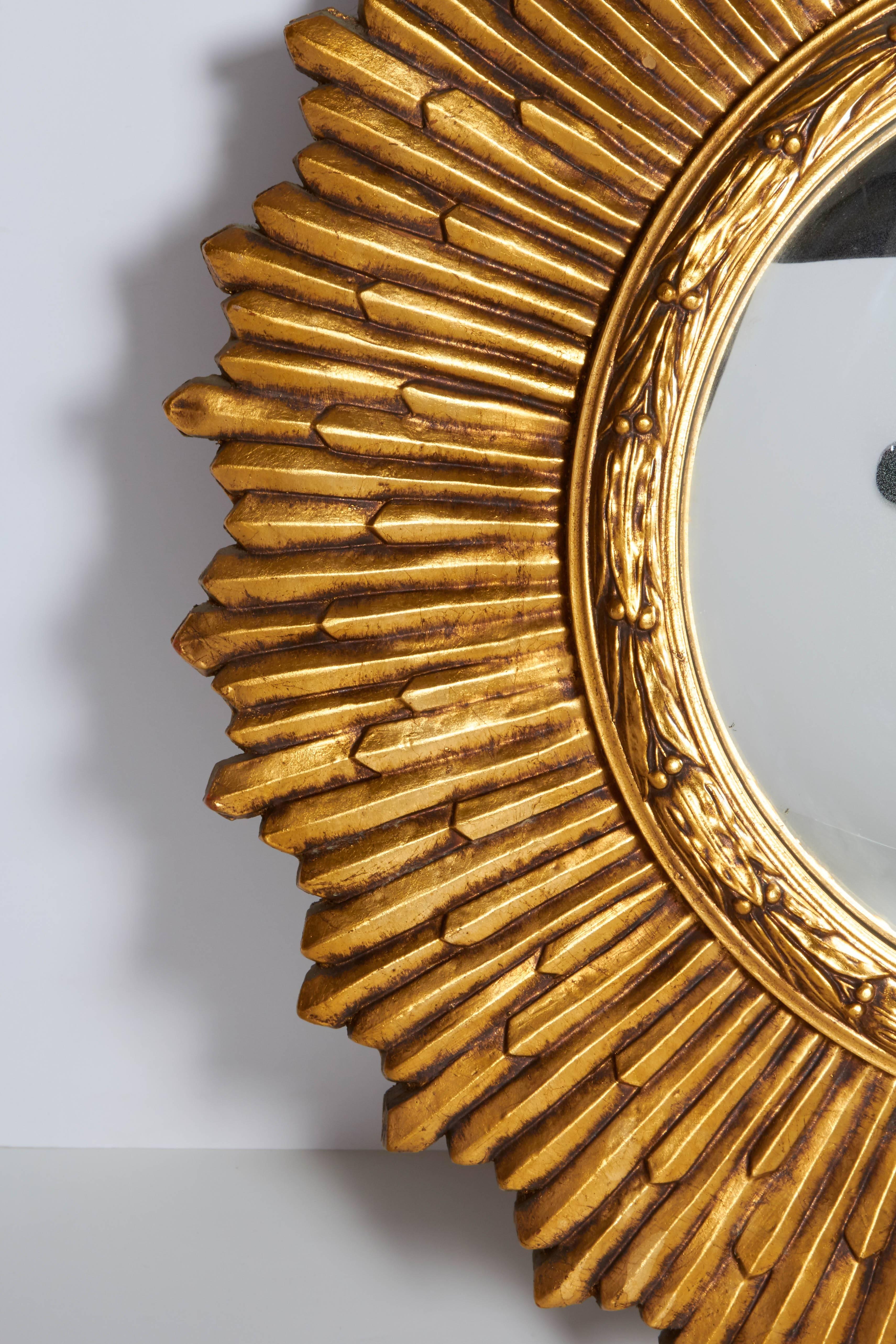 A sunburst mirror, produced circa 1960s, with convex mirror, inset within a carved giltwood frame, with details of bell flowers to the rim, surrounded by staggered rays. This mirror remains in very good vintage condition, with age appropriate wear
