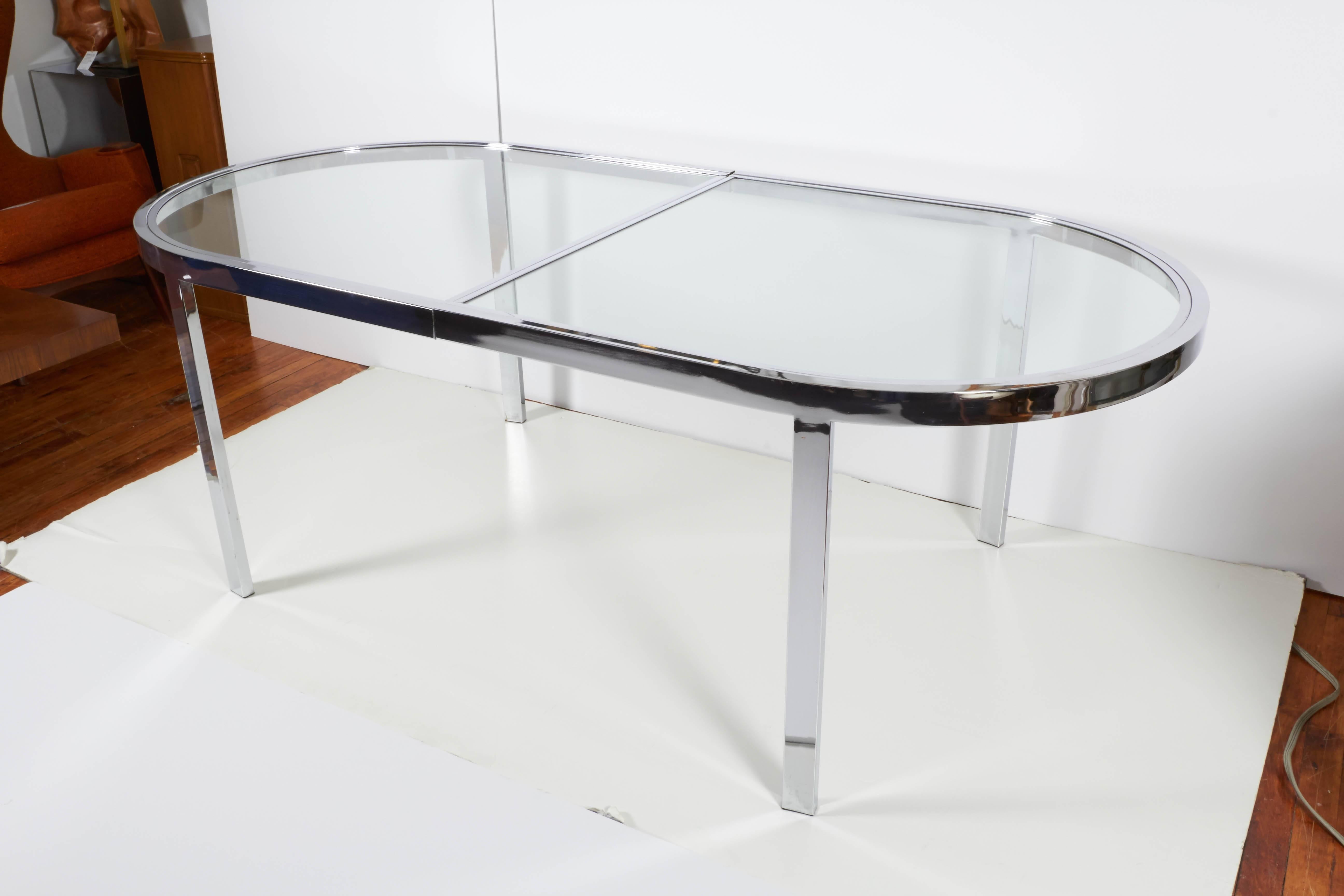 This chic dining table, designed by Milo Baughman and produced circa 1970s, includes glass racetrack top, against a chrome frame, with stepped detail to the perimeter, on linear legs. Very good vintage condition, consistent with age and use.