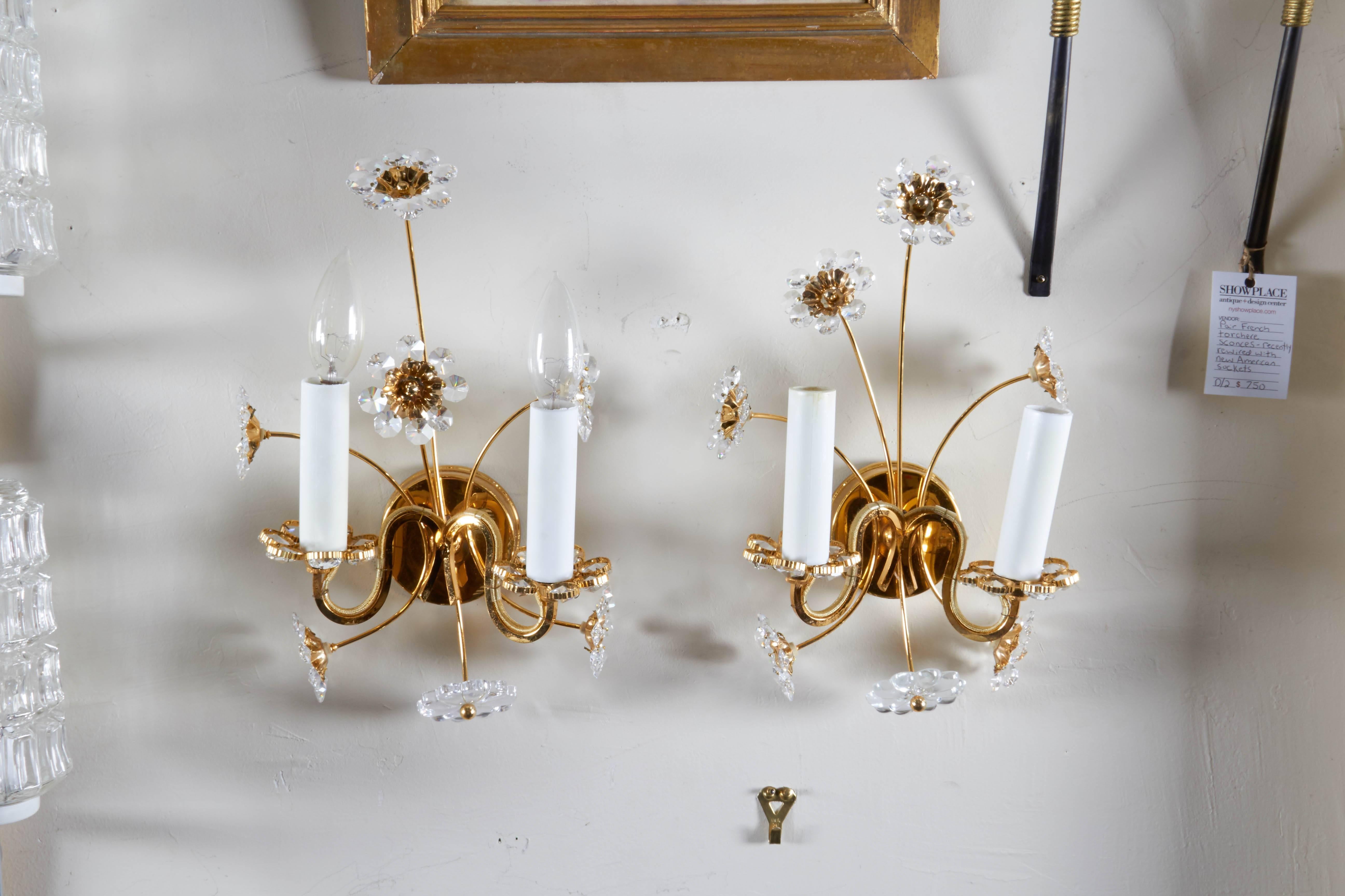 A pair of Palwa sconces, produced in Germany, circa 1970s, each with floral sprays, accented with faceted crystals, and two S-curve arms emanating from round gilt brass wall bracket. Sockets to US standard, both require two candelabra base bulbs.