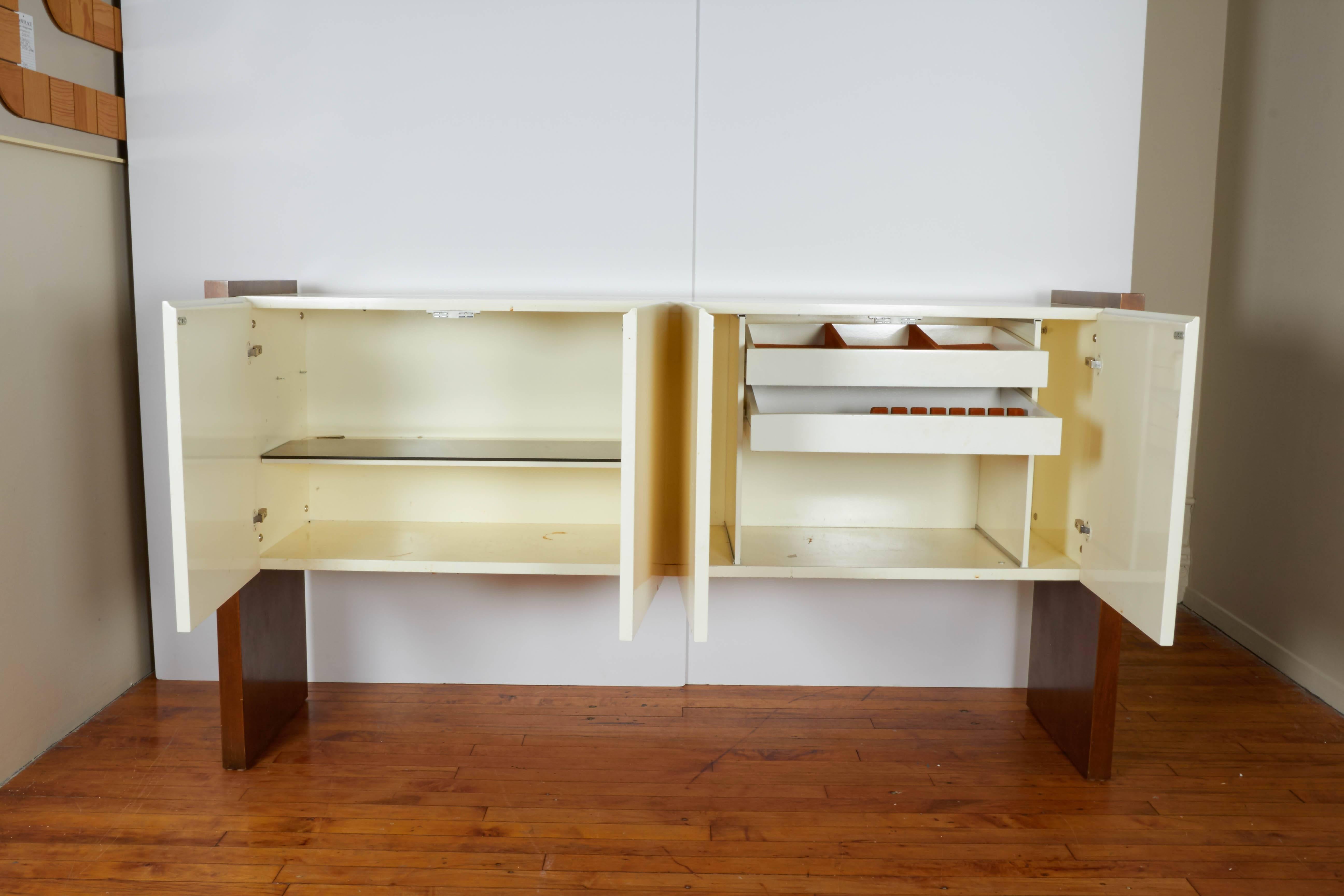 This highly linear Milo Baughman sideboard, produced circa 1970s for Thayer Coggin, includes two white lacquer cabinets, each with double doors, flanked by wood sides as support; interior of cabinets include glass shelf to the left, opposite two