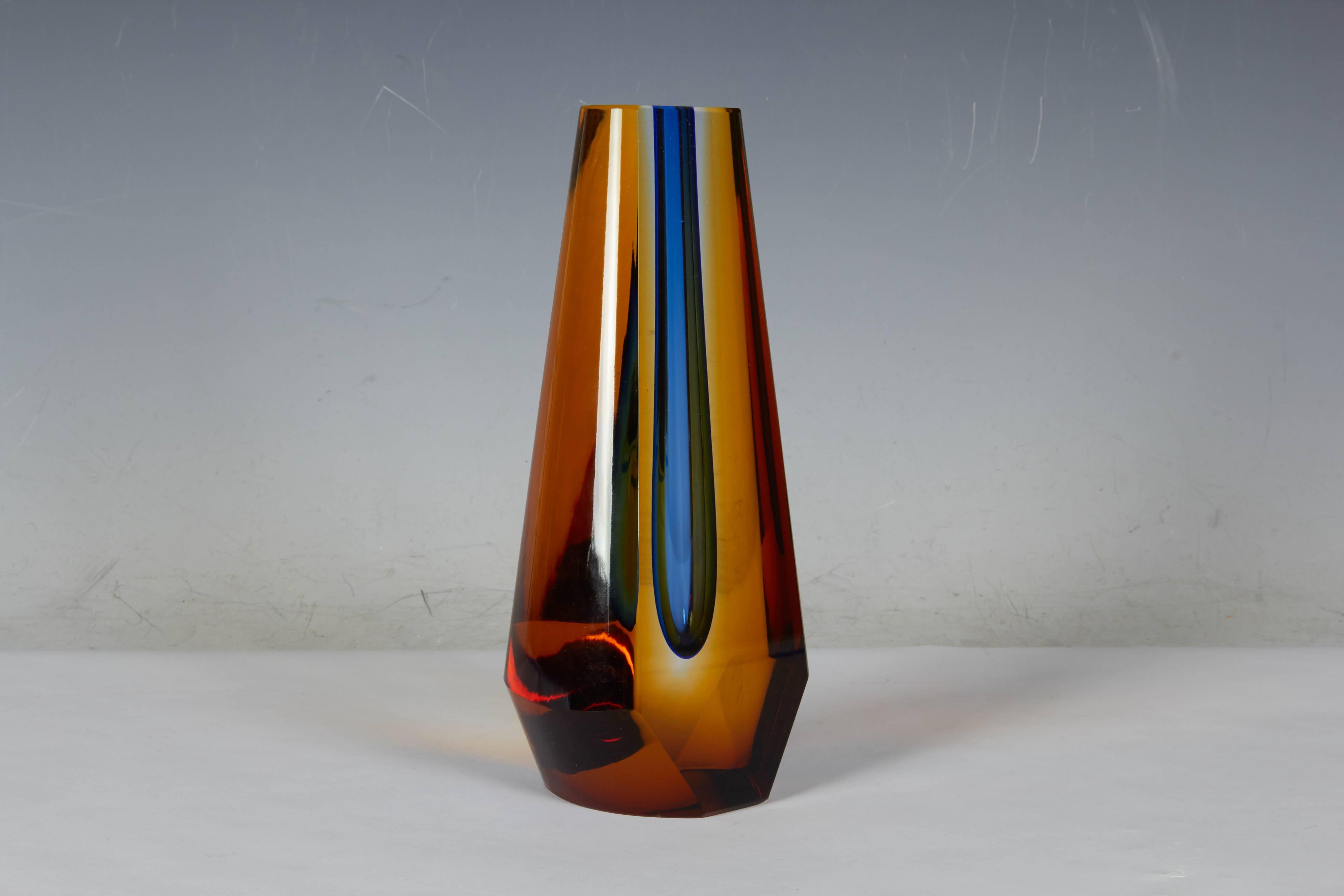 A thick, sculptural glass vase by Czechoslovakian born Pavel Hlava, with tapered and faceted form, comprised of three layers, amber over clear, surrounding a tubular interior in blue. This unique design was created by Hlava for the Milan Triennale