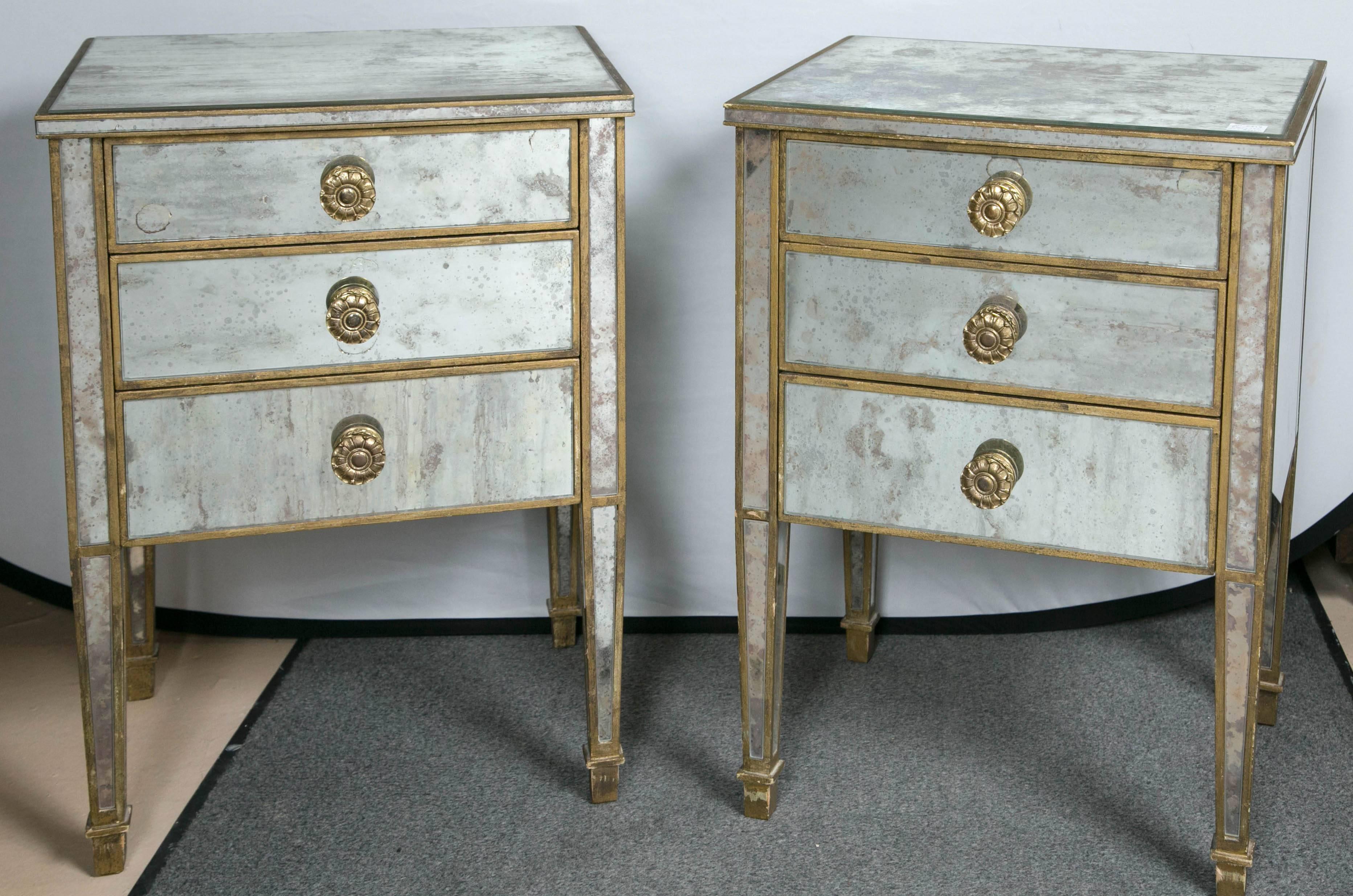 A pair of Regency mirrored night / end tables each having three drawers. The antiqued mirrored case having distressed finish. This fine solid wooden pair add the allure of sleek and Hollywood Regency glamour to any area of the home.