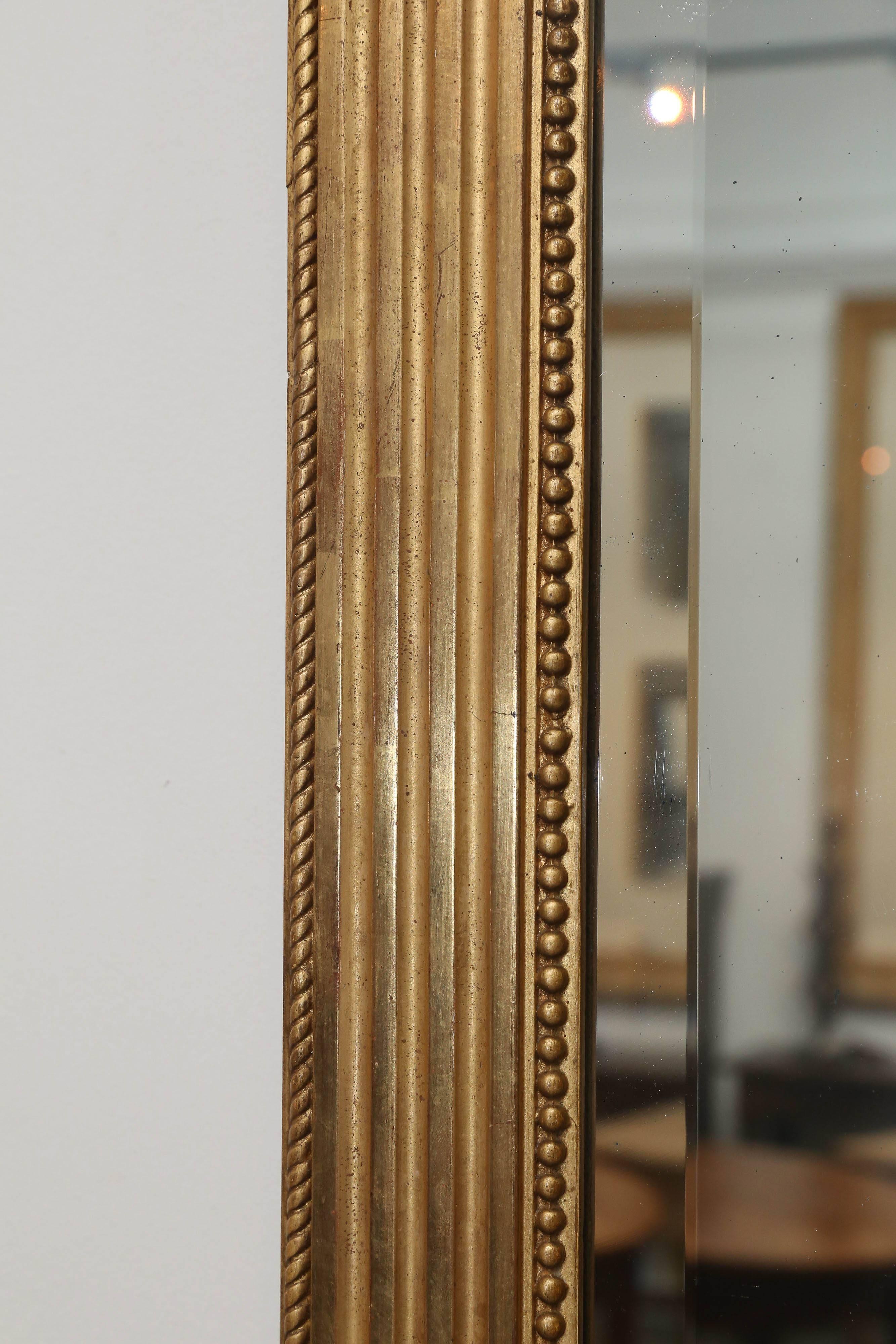 Large gilt reeded antique mirror from France. Pretty detail in each corner and an interior perimeter of pearls. Can be hung horizontally or vertically. Original beveled glass. Original pine board back, circa 1890.