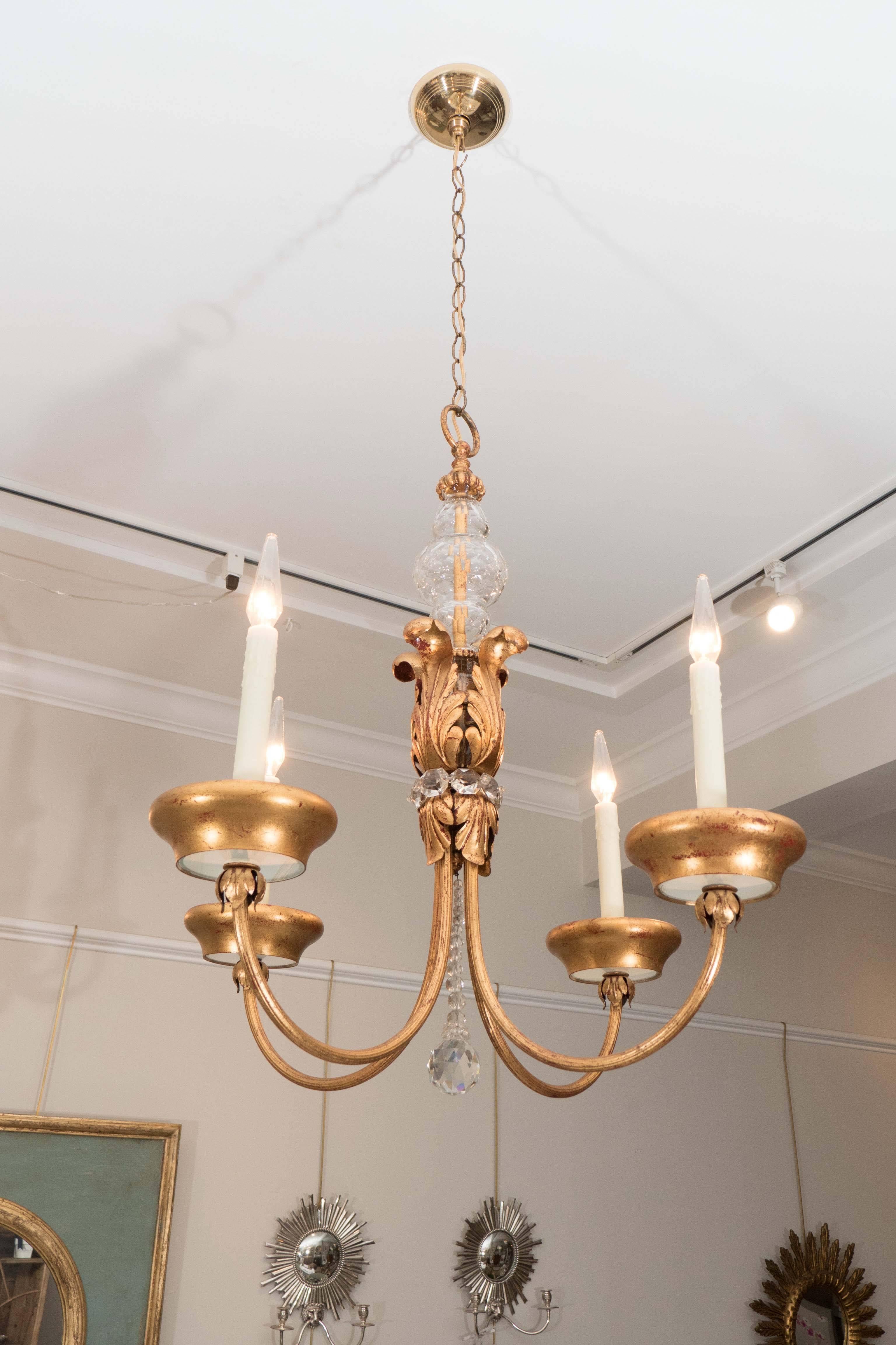 A charming four-arm French chandelier in gilt metal with lovely faceted glass detail at top of chandelier and a glass ornament suspended by a beaded chain at base. The four arms stem from a center scrolled-leaf center ornament surrounded by glass