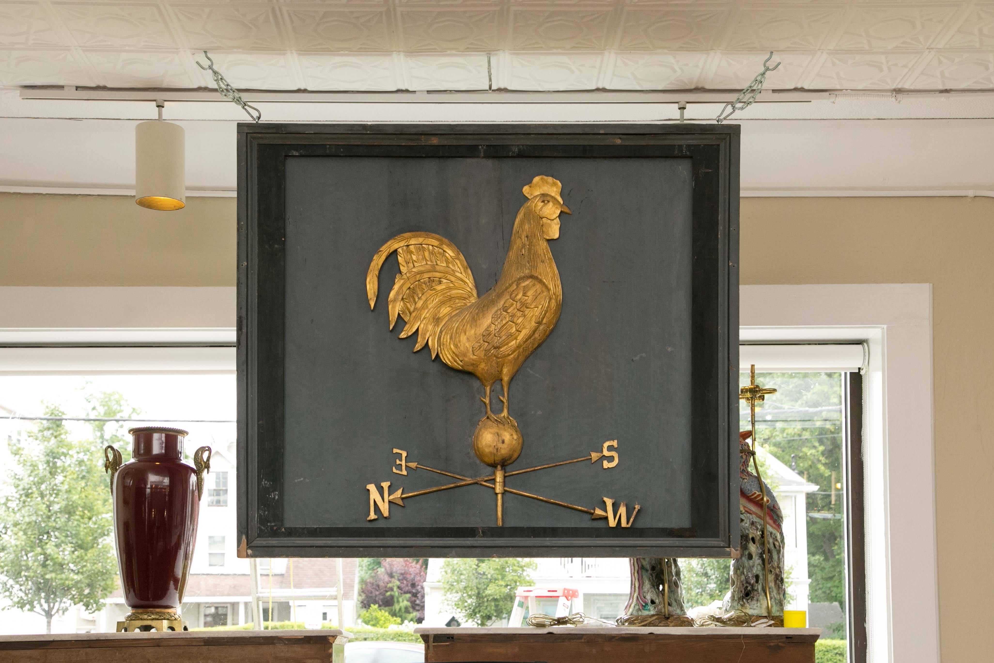 A very large solid painted wood decorative art piece (possibly a pub sign). Both sides display a three dimensional giltwood rooster weathervane in relief. The piece hangs from the top and is set in a deep double edge frame.