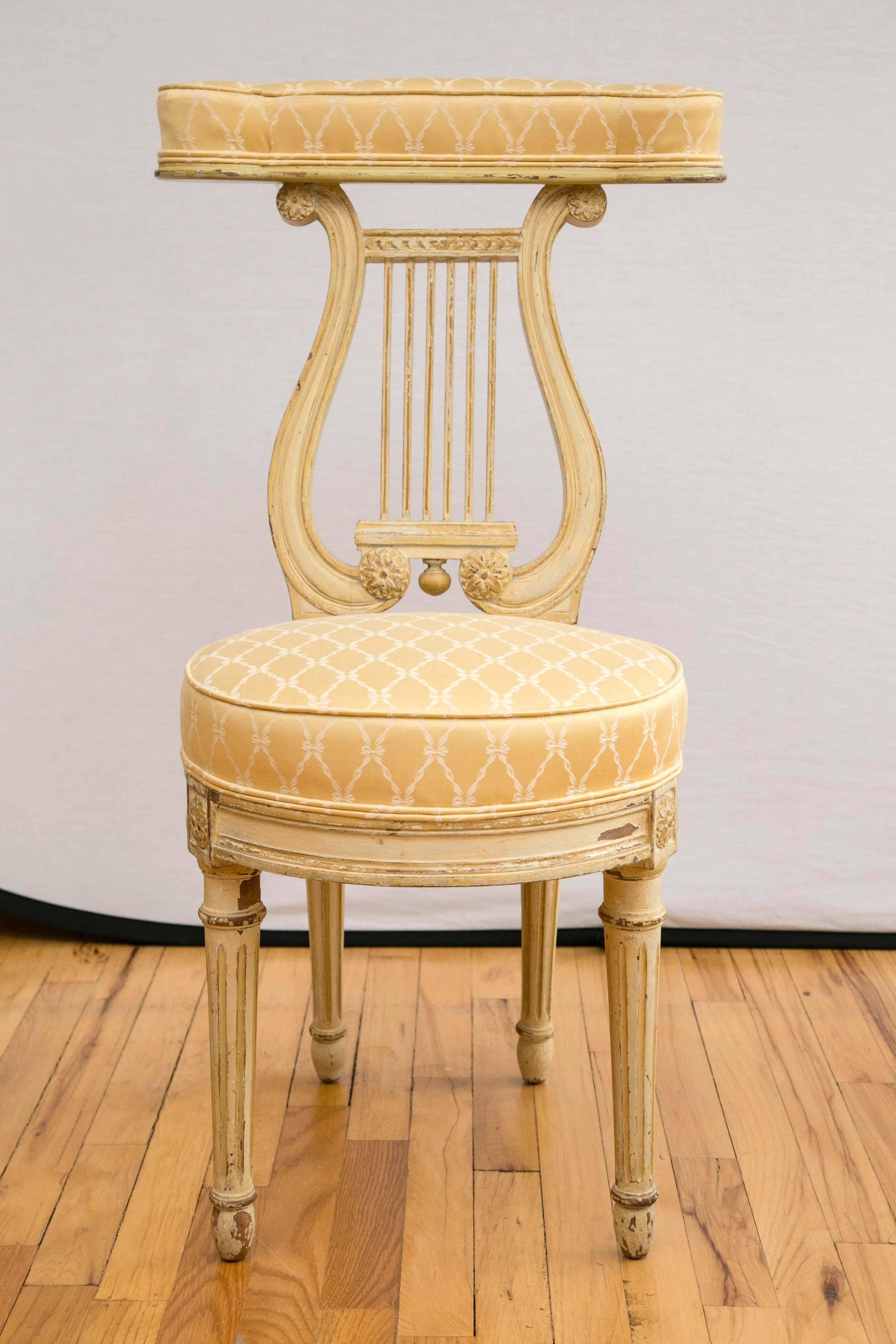 A cream painted wood, yellow upholstered voyeuse. A chair on which a 