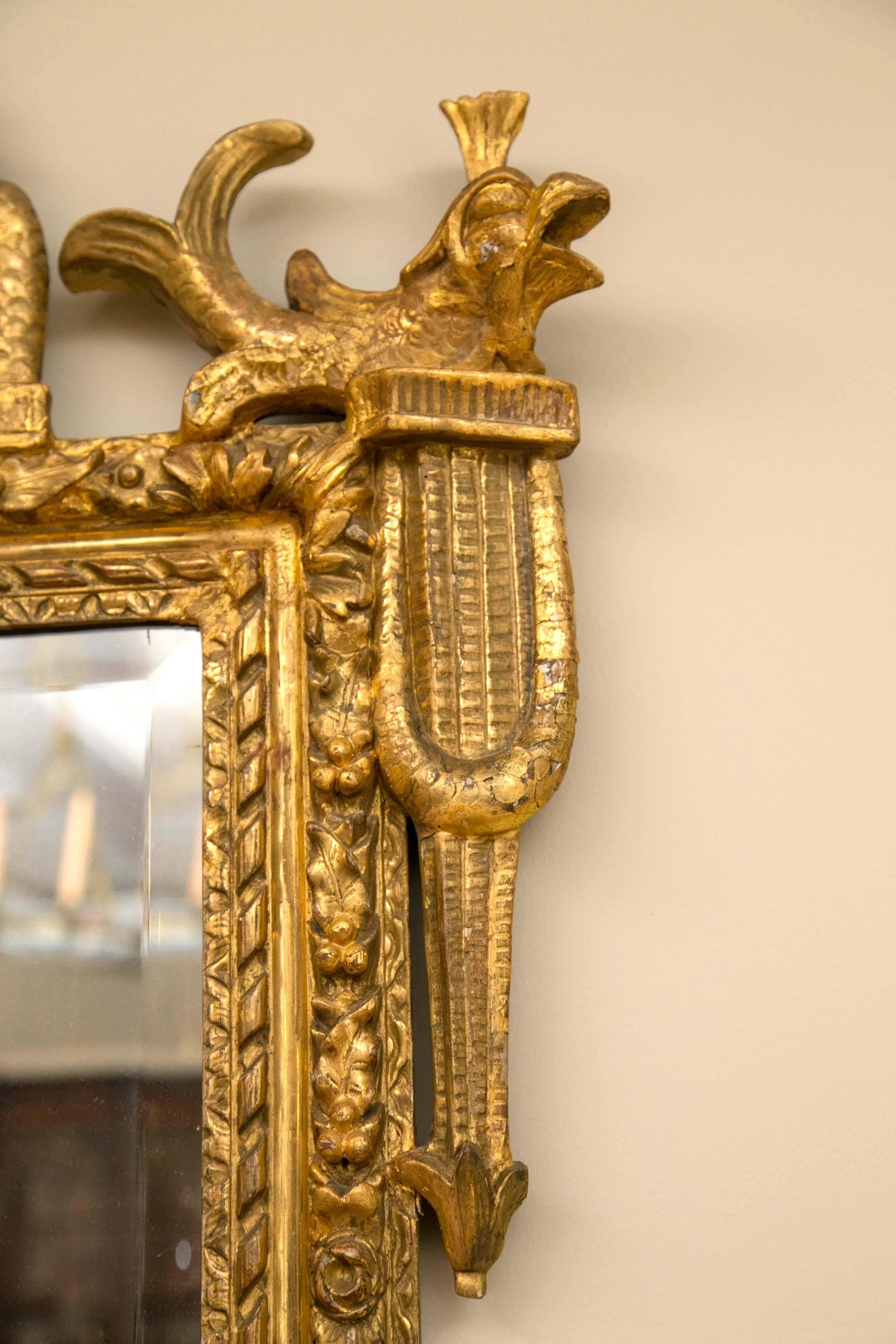 Elegant miroir français de la fin du XVIIIe siècle, sculpté à la main dans du bois doré de l'époque du répertoire Louis XVI. Le plateau est sculpté d'oiseaux et de fleurs, les bords sont ornés de dauphins sculptés, le cadre est orné de rosettes et