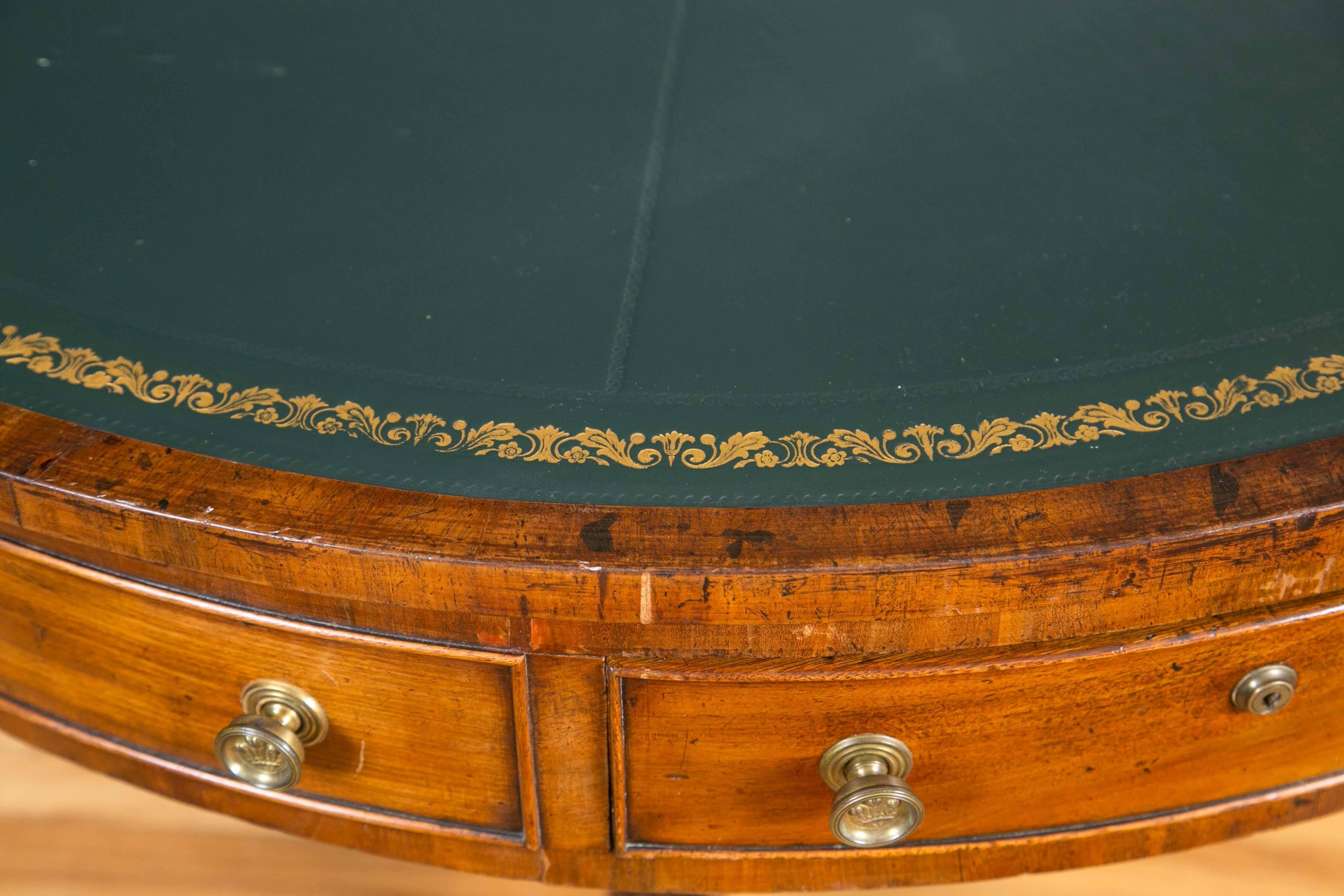 The circular top with gilt-tooled, green leather surface above four pull-out frieze drawers and four simulated drawers. The top sits on a turned pedestal base with three reeded and splayed legs that terminate in brass caps and castors.
 