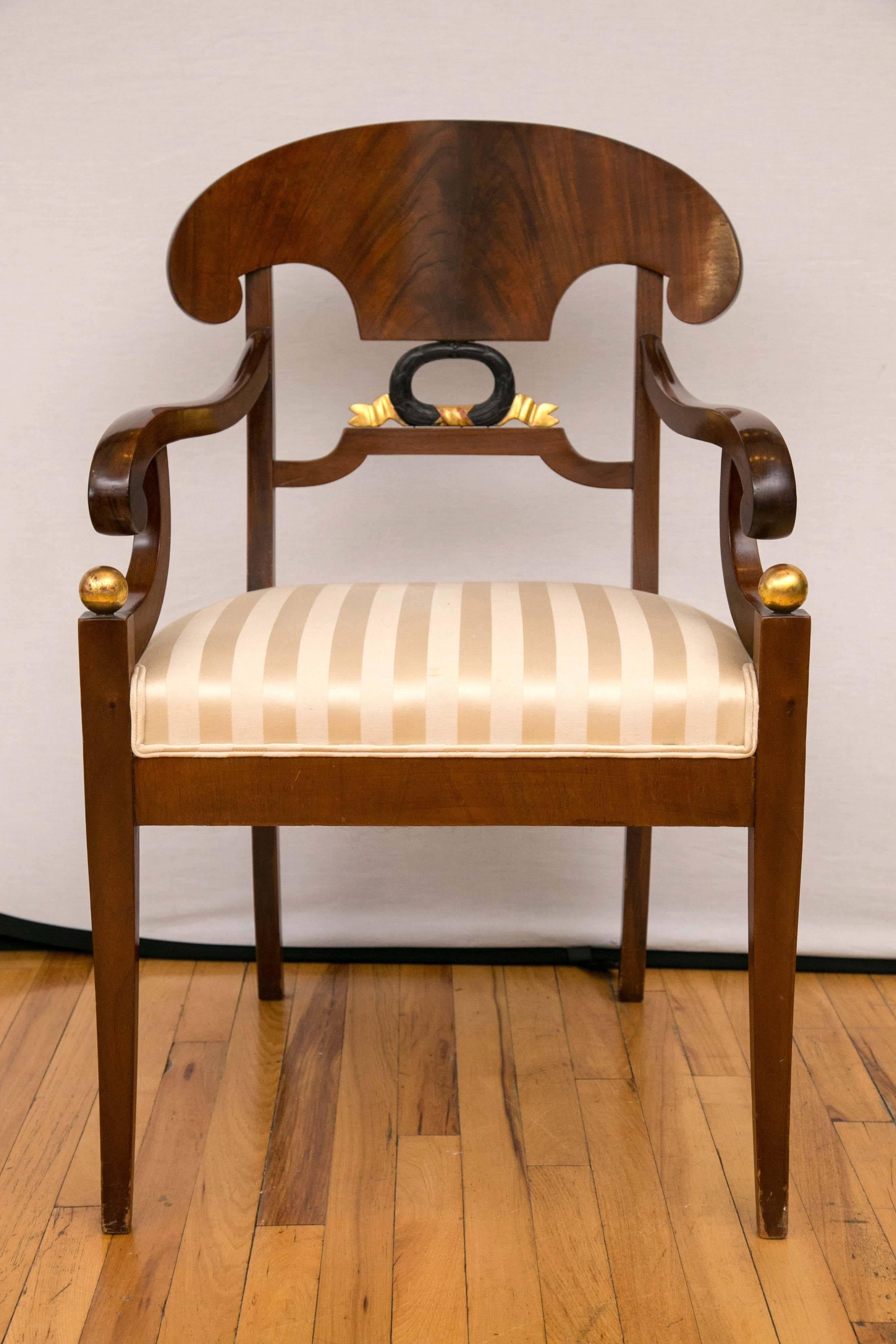 An exquisite pair of armchairs. This pair of Biedermeier armchairs feature fountain form back, scrolled arms joining the from legs topped with a gilt ball motif. The armchairs are raised on four saber legs. Wonderful rich color.
