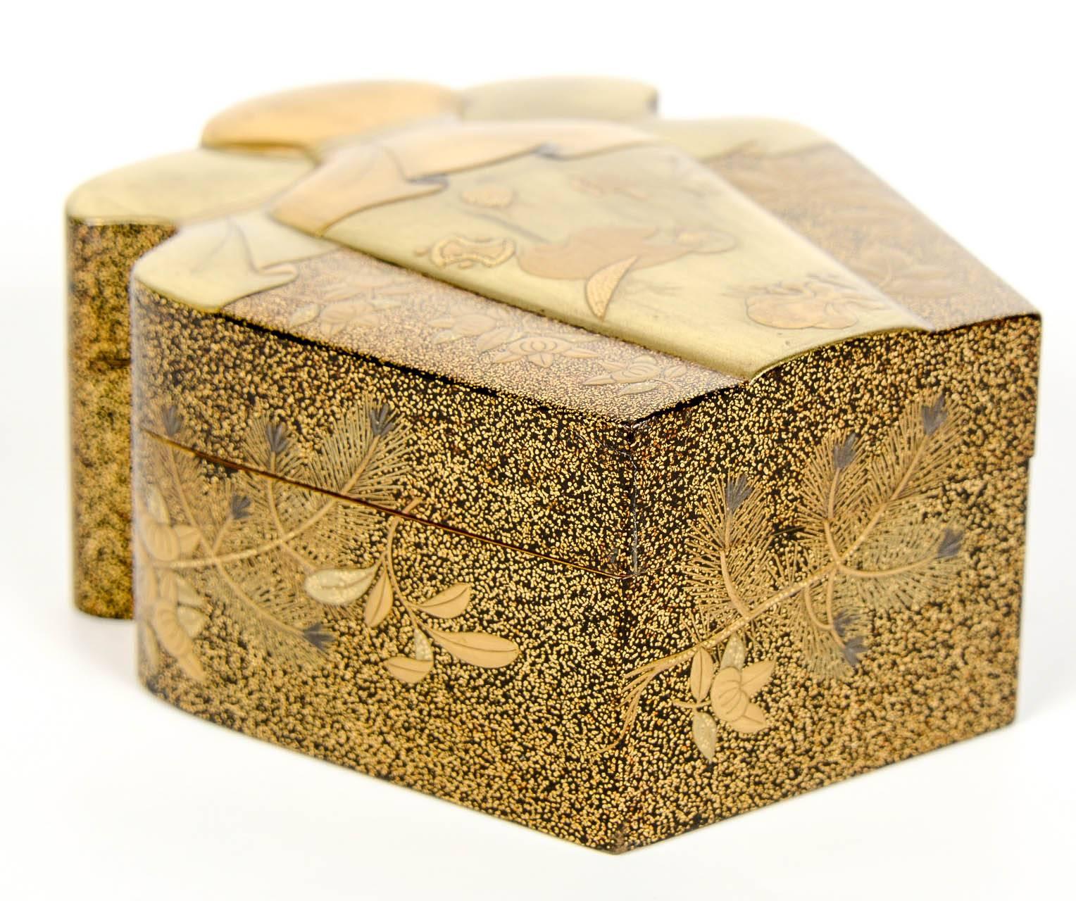 Small gold lacquer Kobako depicting a purse tied by a cord. It shows a ritual objects decor in its central part, flowering branches and pine trees on the sides of the lid.
The sides are decorated with flowering branches and pine branches on a