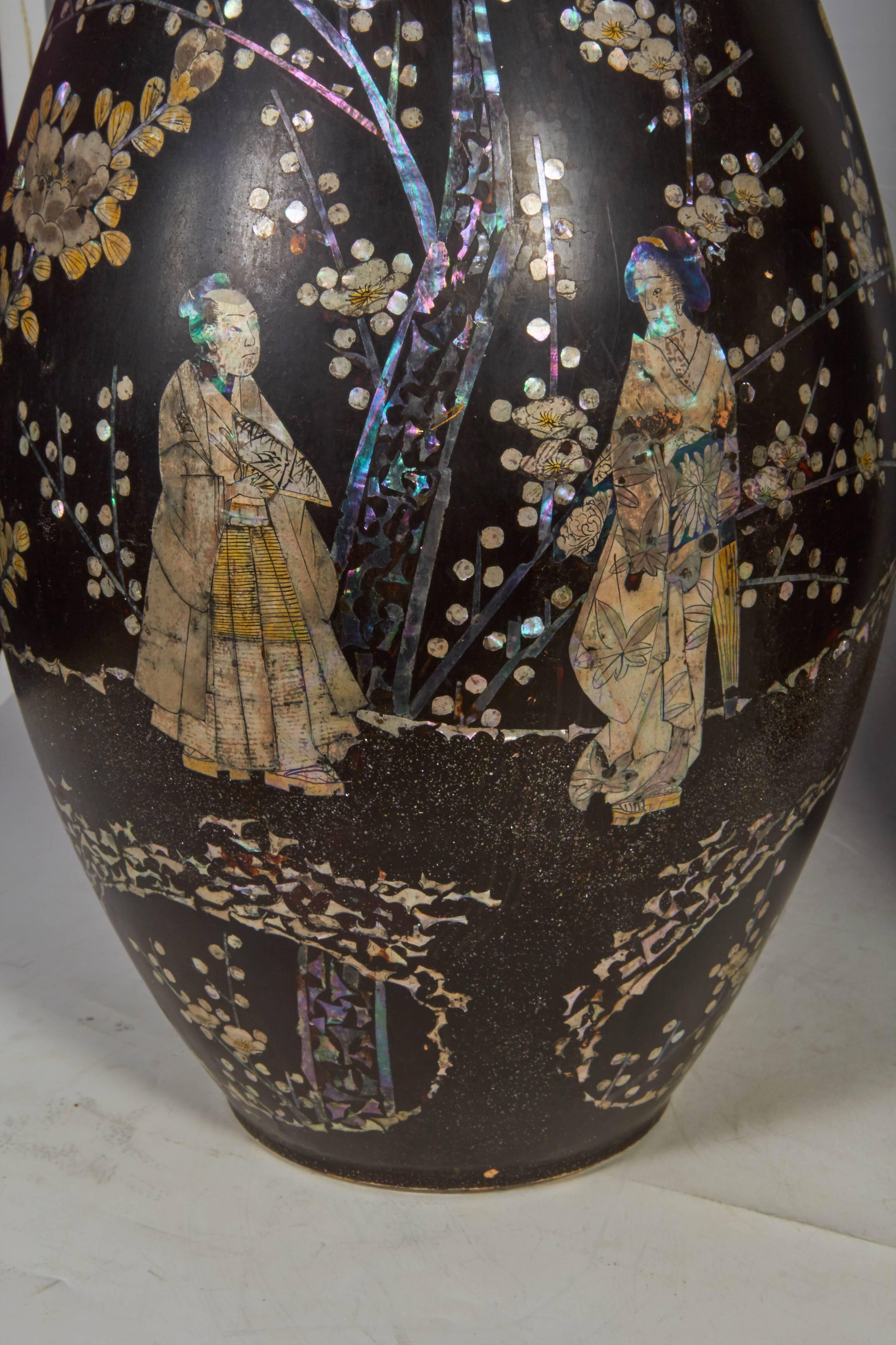 A very unusual and rare pair of Japanese black porcelain mother of inlaid chinoiserie decorated vases, each depicting Chinese/Japanese figures in a garden full of flowers, decorated and inlaid with polychrome mother-of-pearl and gold highlights,