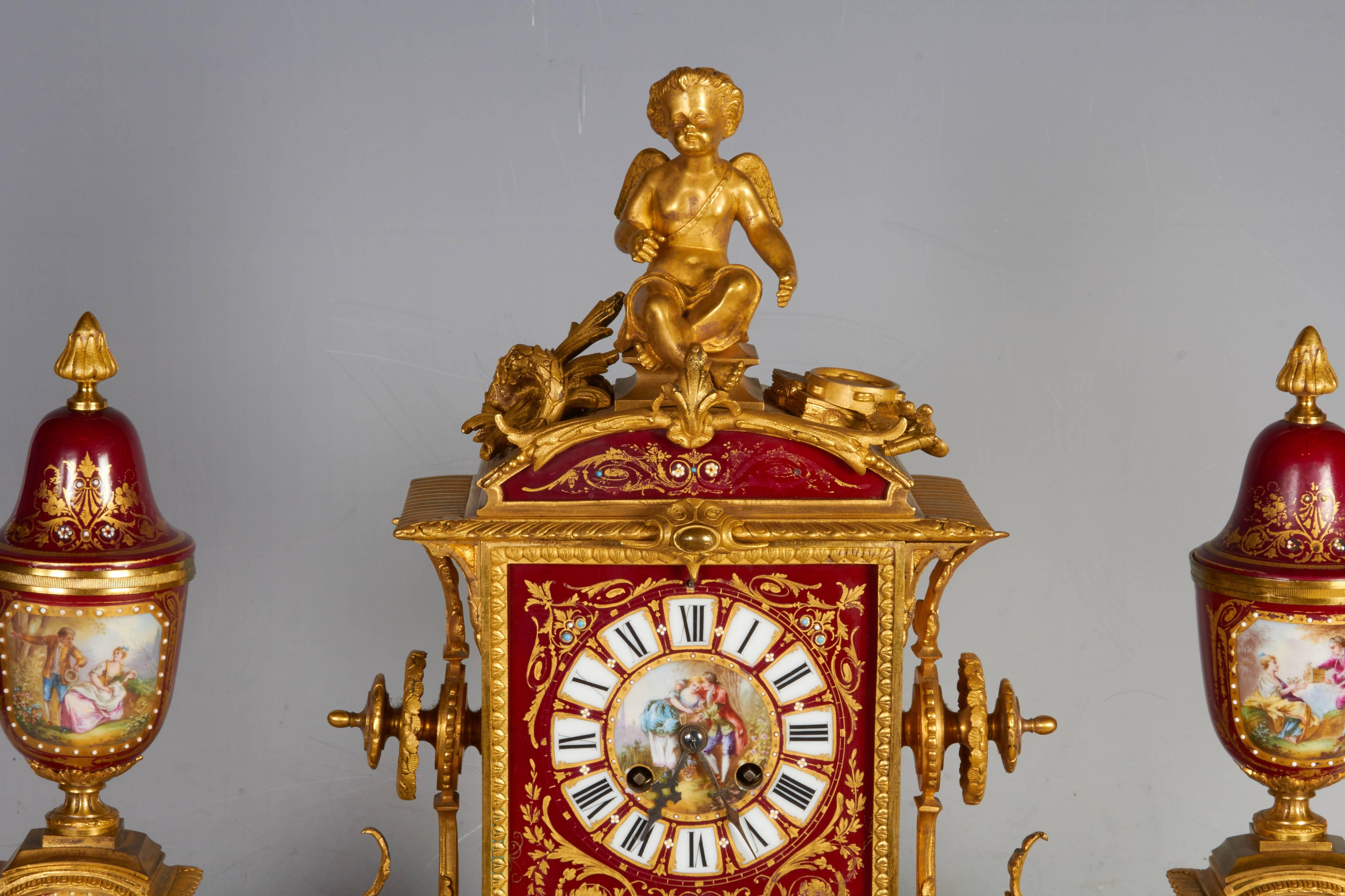 A very fine antique French ormolu-mounted Sevres style ruby ground, jeweled and enameled, three-piece clock garniture, each finely painted with Watteau scenes with lovers in landscapes and scenes galantes within 24-karat gold and raised jeweled