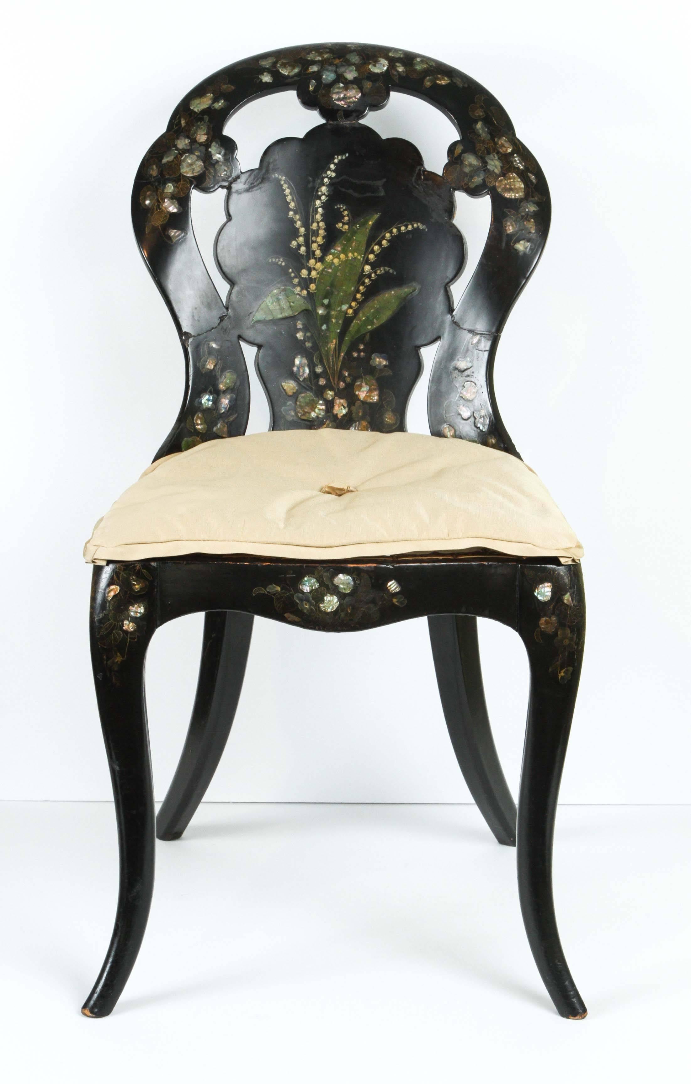 A Papier-Mache chair in black lacquer finish with mother-of-pearl inlay details (including a charming spray of Lily of the Valley) , circa 1850. The seat is newly caned with a squab cushion in Suzanne Rheinstein Hollyhock for Lee Jofa 