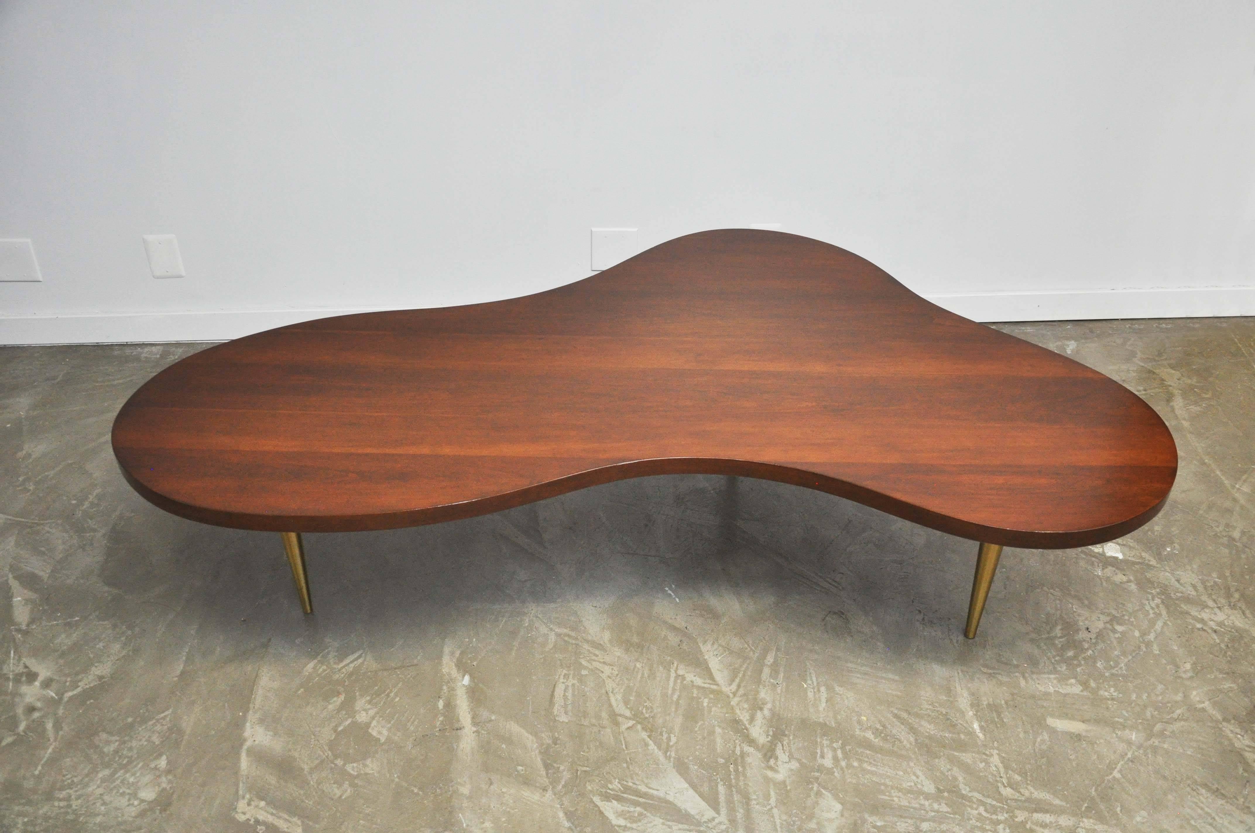 Early walnut biomorphic free-form coffee table with tapered brass legs designed by T.H. Robsjohn-Gibbings for Widdicomb, circa 1950s. Labeled. Very rare monumental scale at 72