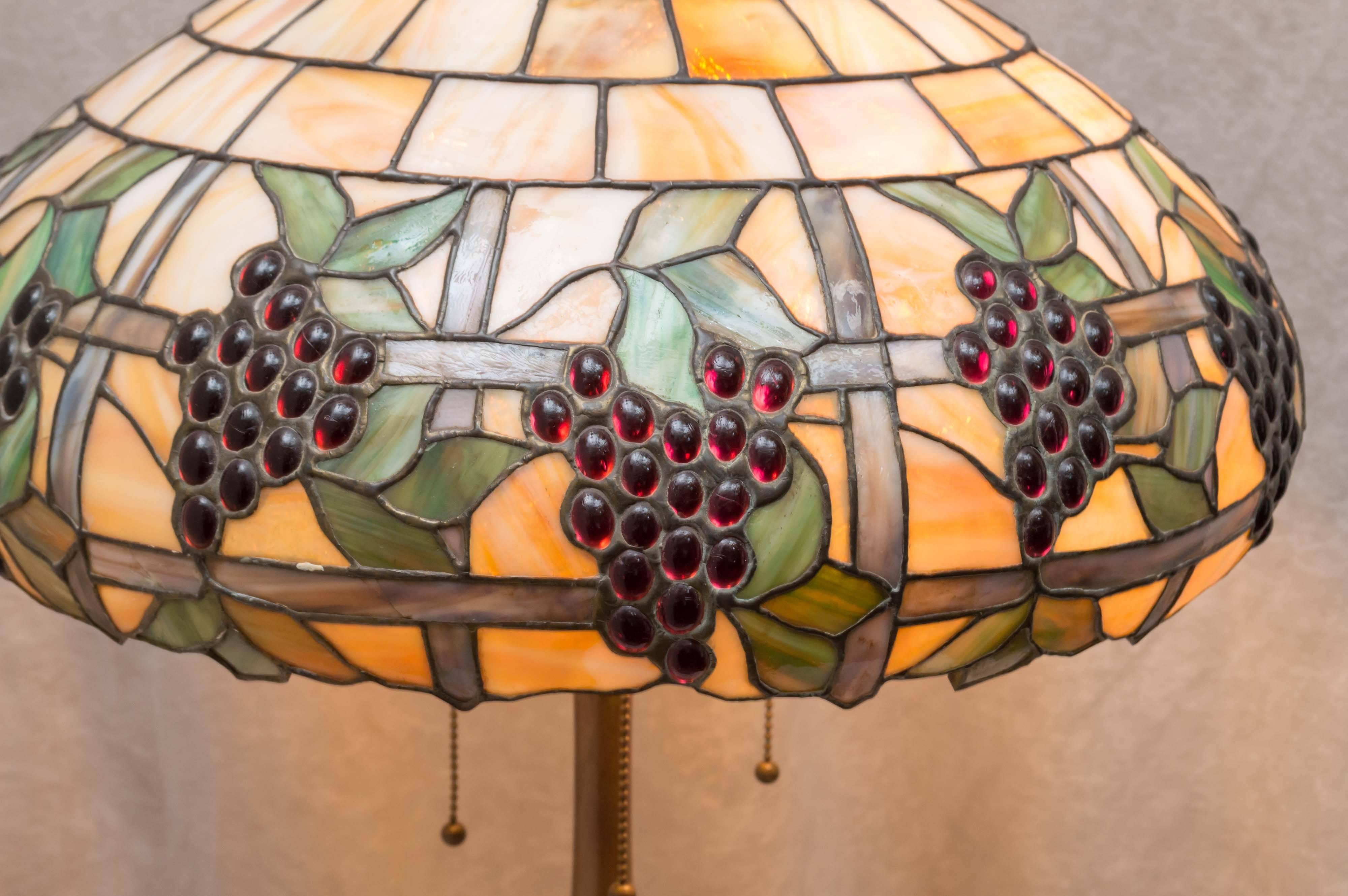 This colorful and high quality table lamp is a fine example of leaded glass lamps. The shade has many bent tiles and colorful grapes that extend beyond the other design. The base is bronze, is cast and heavy. Not the cheap thin metal. We have