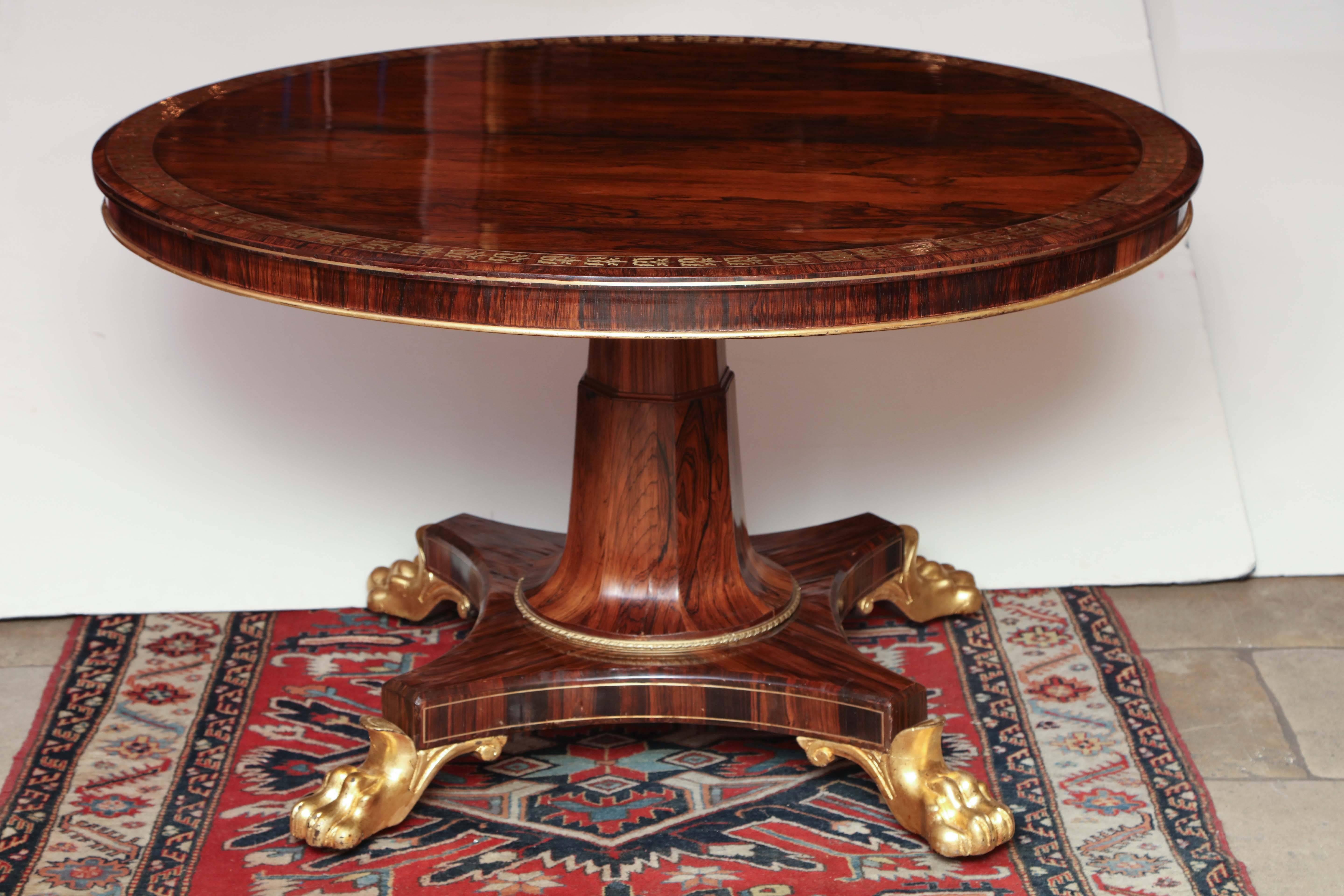 A fine Regency brass inlaid rosewood tilt top center table with rosewood pedestal base and carved lion paw feet.