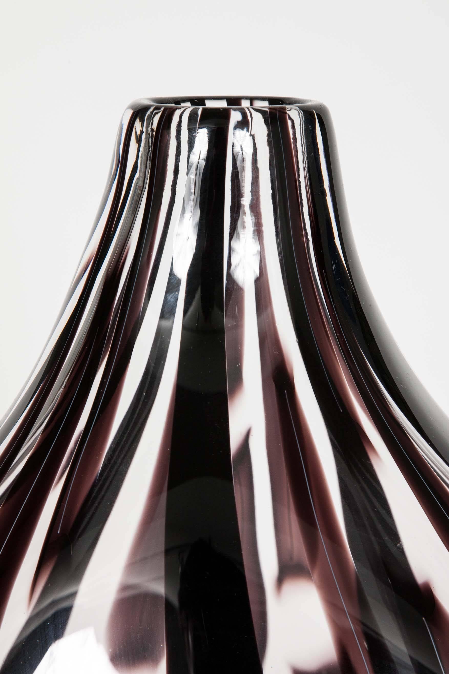 Ikate II is a unique handblown clear and aubergine/dark brown /black, glass sculpture by the Swedish artist Ann Wåhlström. Created to form an elegant teardrop shape, finishing in a refined thin neck, canes of dark coloured glass appear woven into