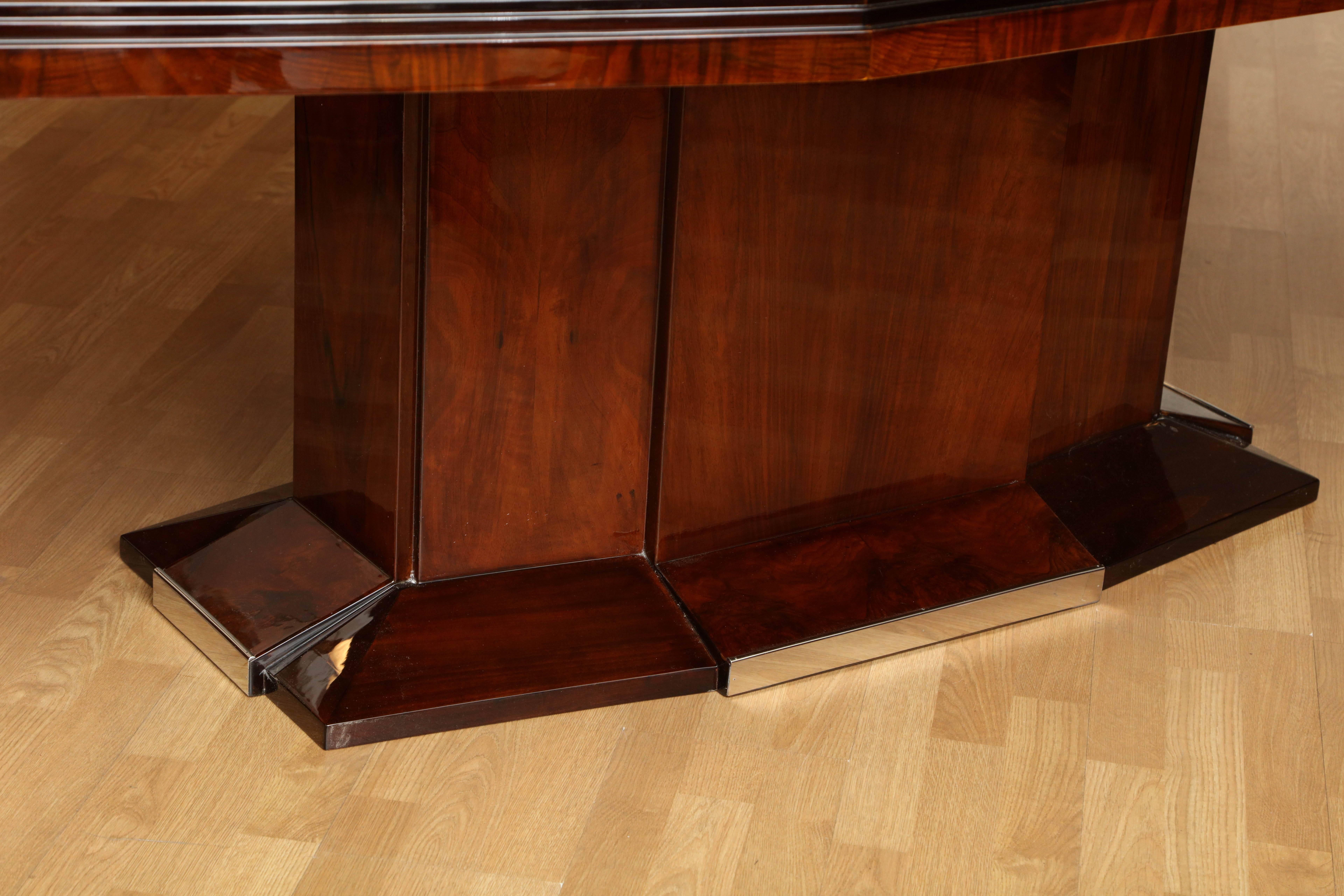 Grand Art Deco dining table. Black Forest walnut with polished nickel detail at base. Includes two finished 20 inch extensions. In the manner of Dominique.