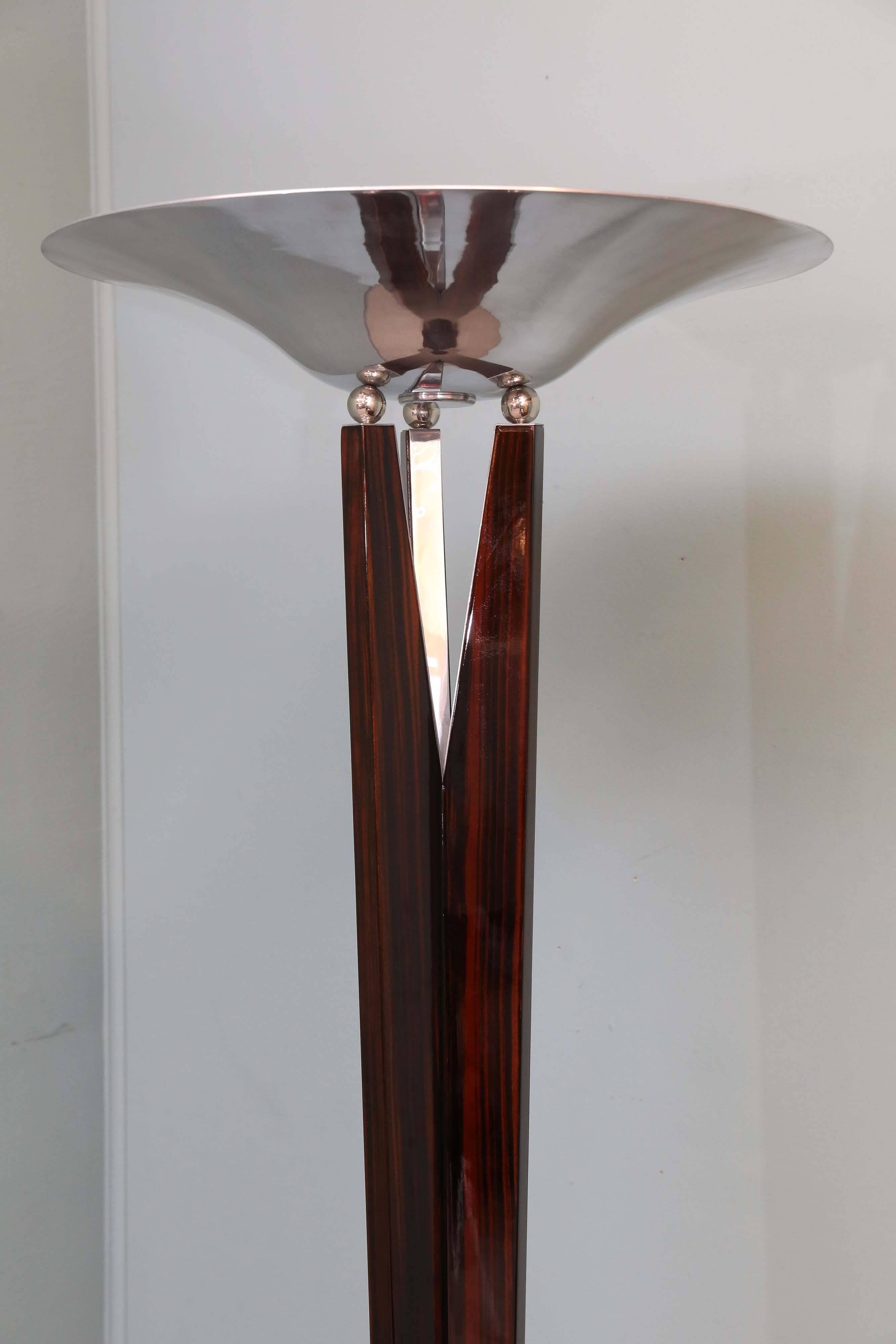 The wooden thick stable base of the lamp supports three rectangular poles that are connected with each other. Right before the funnel shaped chrome lampshade, the poles are distanced from each other and providing better support for the lampshade. On