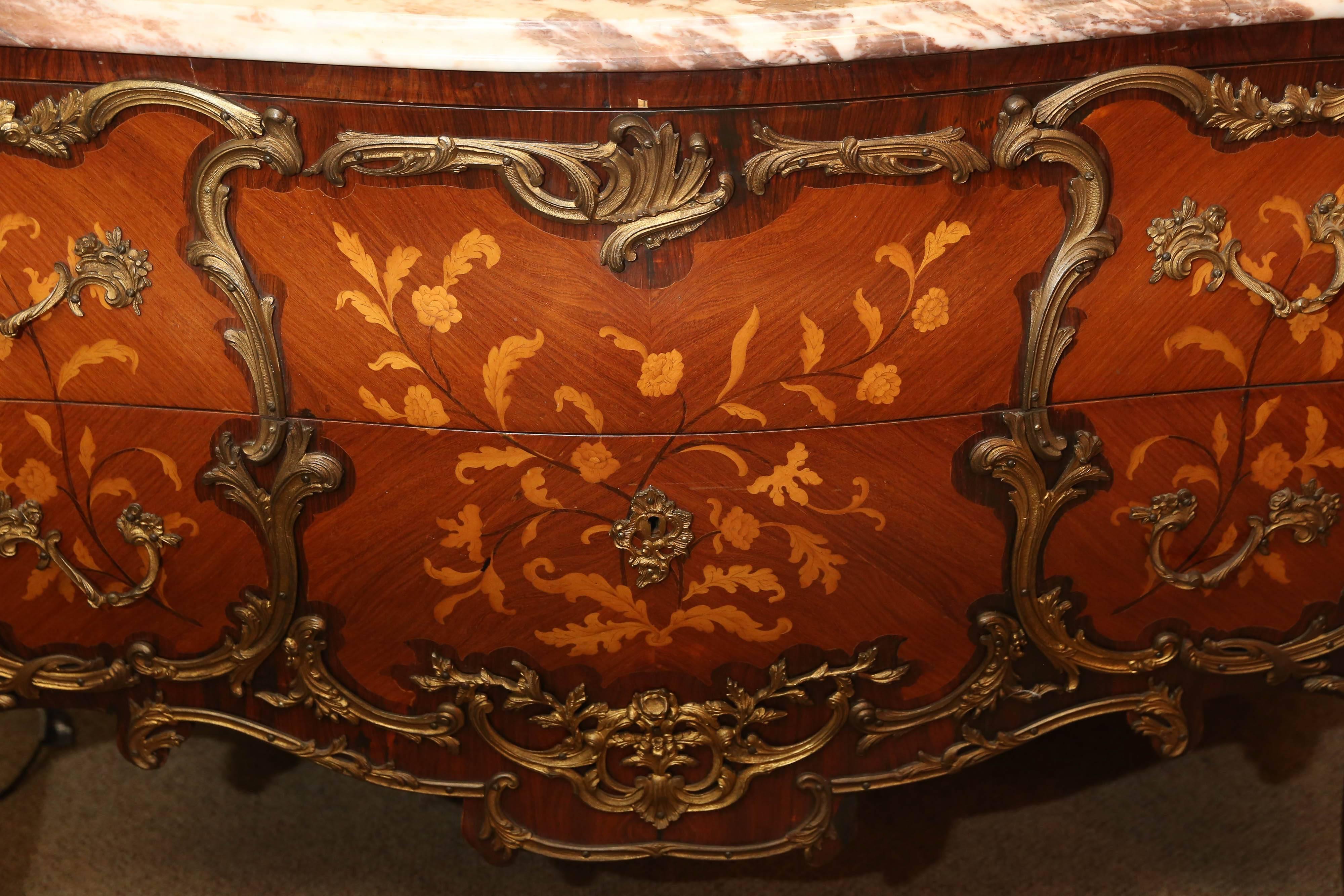 Pair of French commodes with marble in shades of pale violet and cream
color. They are inlaid in a foliate design and the wood is a combination
of kingwood, tulipwood and walnut. Ormolu bronze mounts surround
The foliate design and mounts of a
