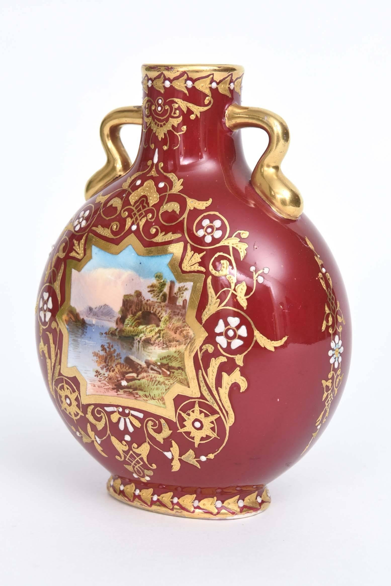 A charming vase by the storied English firm of Coalport. This sweetie features 2 handles, and an interesting hand painted scene with river, mountains, flora fauna accented with white jewels and raised tooled gilding on a rich ruby red ground. Custom