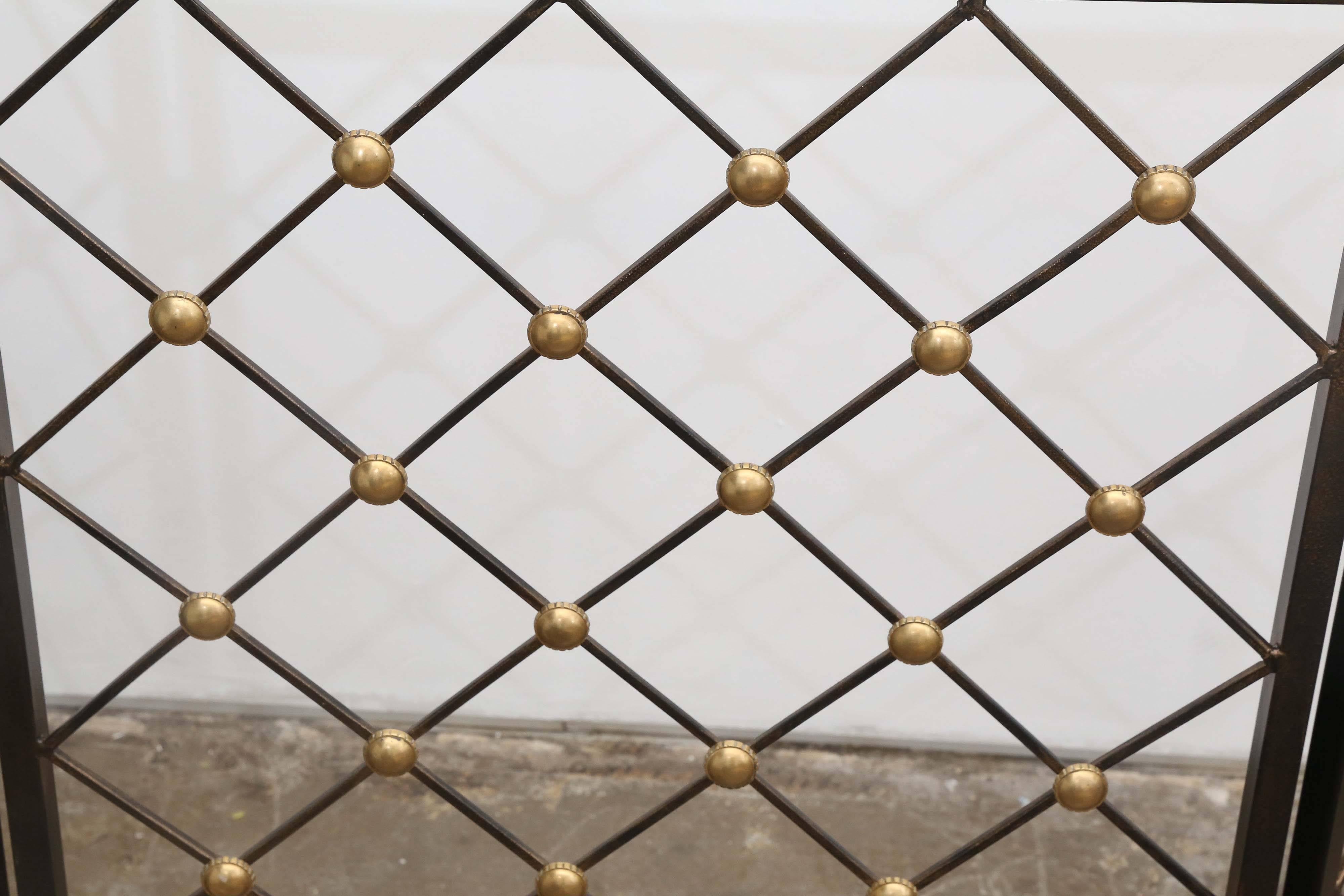 This elegant lattice pattern three panel folding fire screen in classic black patinated wrought iron punctuated by polished brass bosses exudes the refinement and restraint found in the works of classically trained Mid-century modern designers such