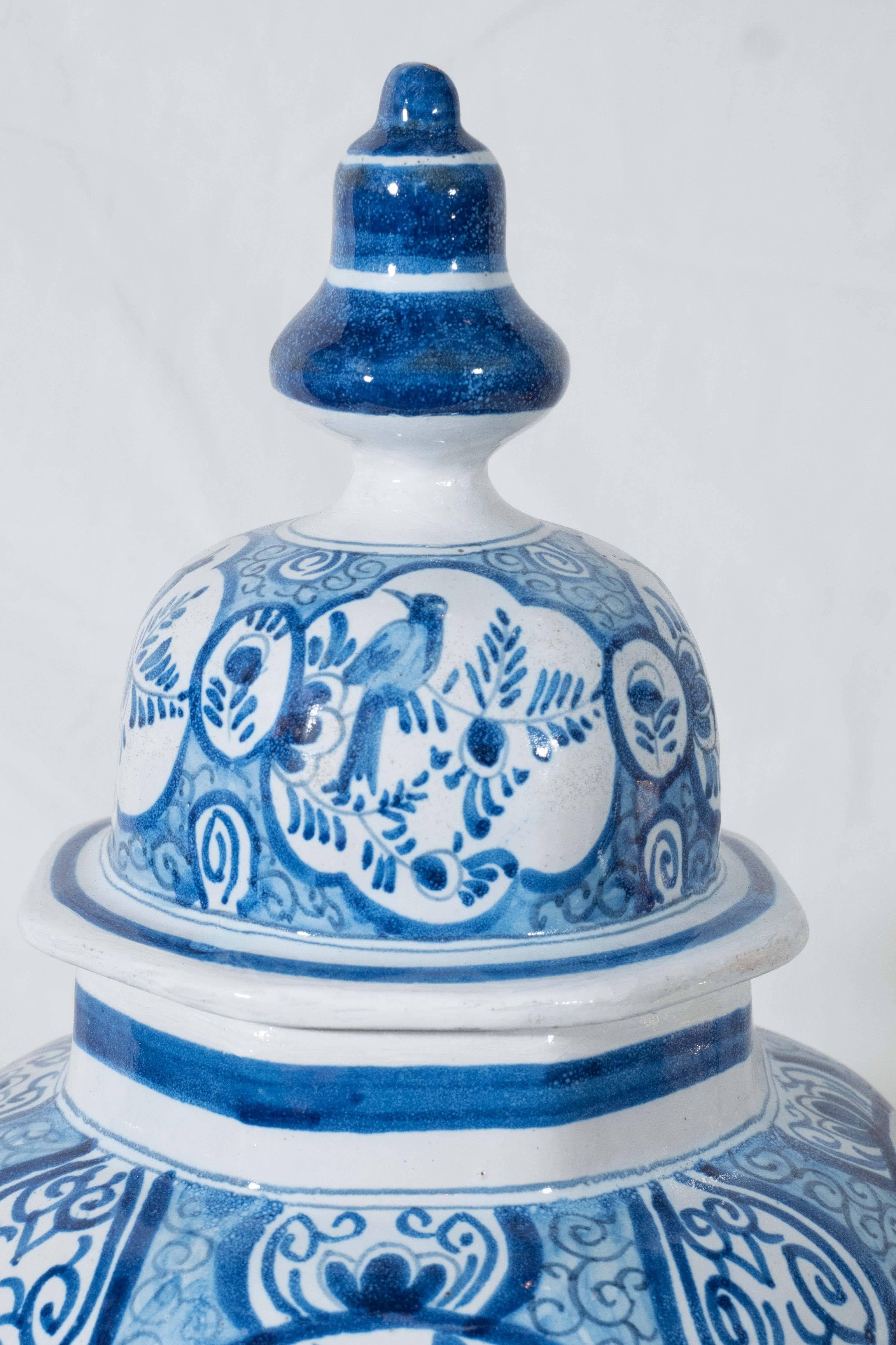 A pair of Dutch Delft blue and white covered jars painted in cobalt blue. Decorated with chinoiserie scenes showing a songbird on a branch, a garden fence, and a Mandarin walking in the garden.