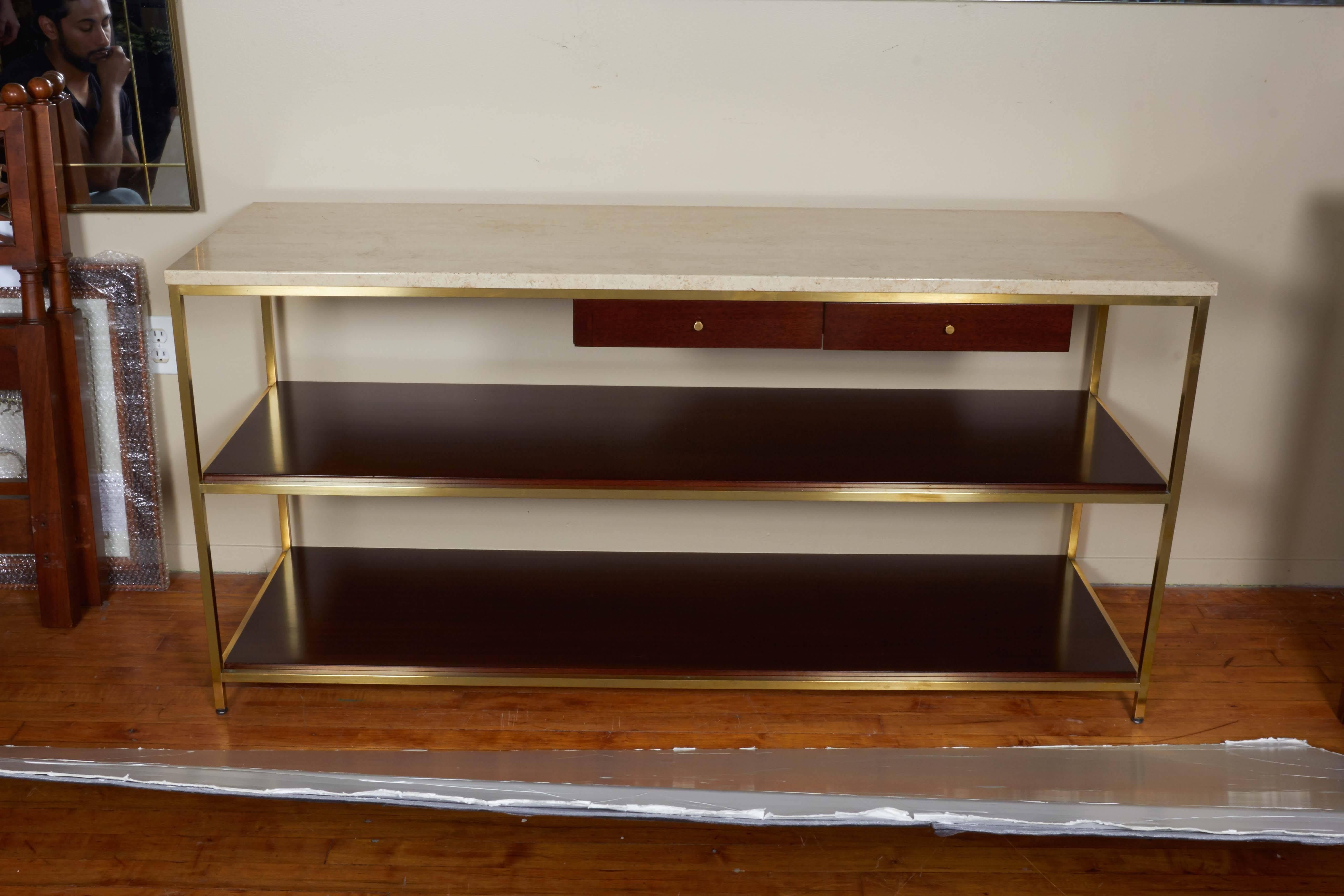 A Paul McCobb console designed for Calvin Furniture's Irwin Collection, produced, circa 1970s, including the original travertine marble top on brass frame, with two wood shelves and two exterior drawers, each with brass knob pull. Markings include