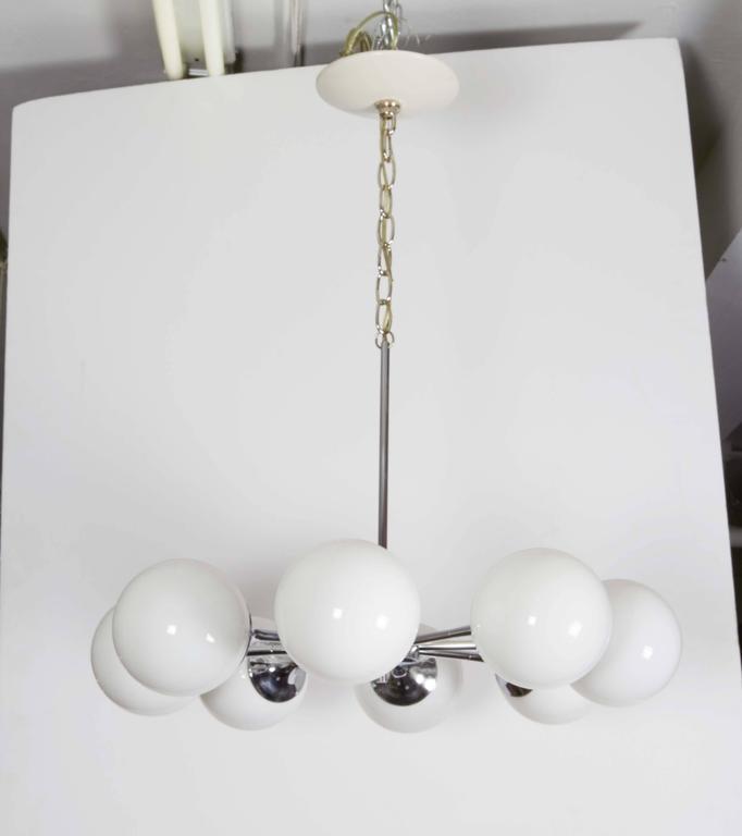 A pair of vintage Lightolier chandeliers, manufactured, circa 1960s in polished chrome with eight trumpet arms, each fitted with the white opaque glass globe spheres, surrounding the sockets. Wiring and sockets to US standard, both chandeliers