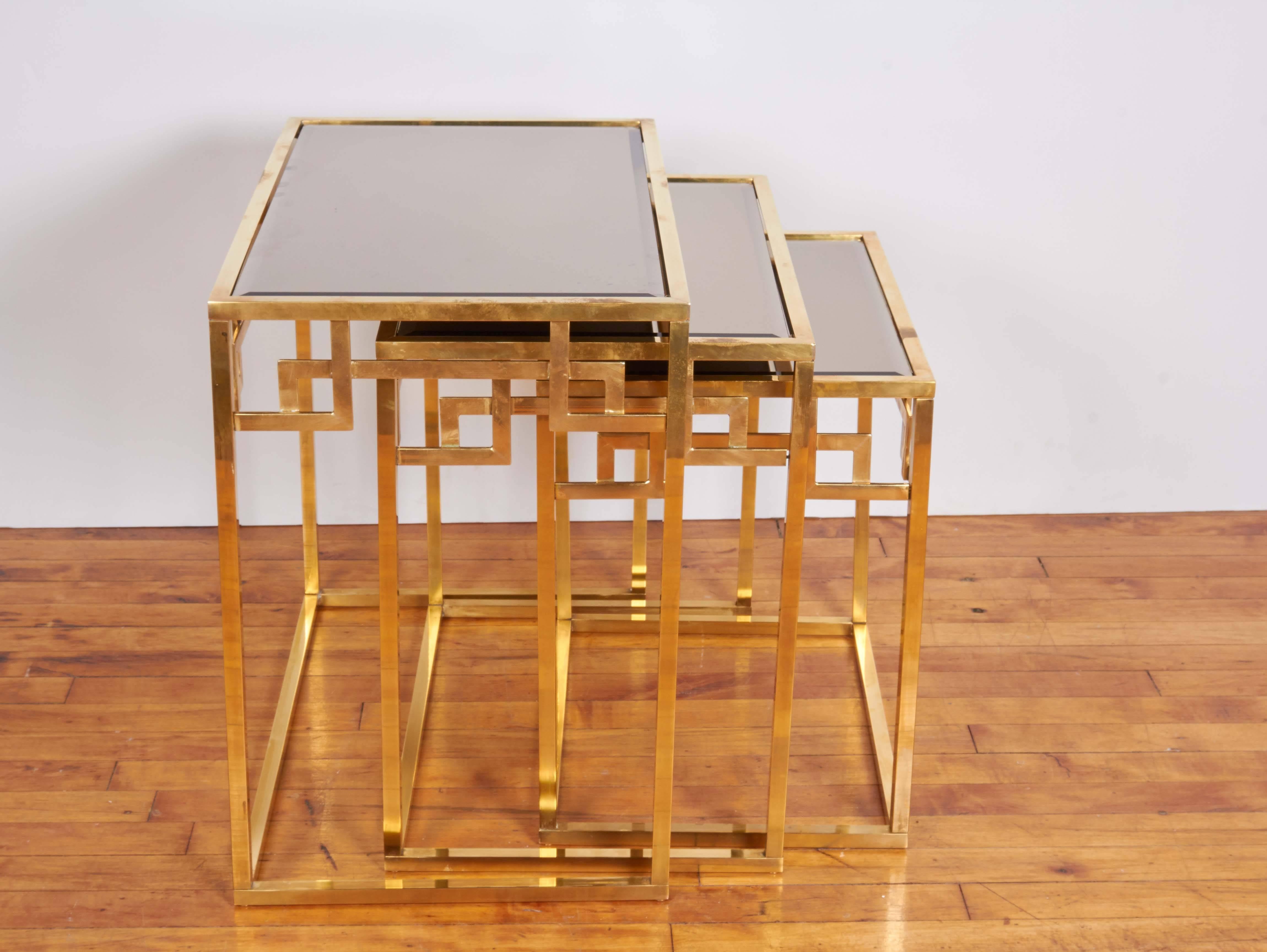 An arrangement of three nesting tables, manufactured in Italy, circa 1970s, each with bronzed beveled mirrored tops, against brass frames, sides flanked by Greek key motifs. Markings include [Made in Italy] label to one of the tables. Very good