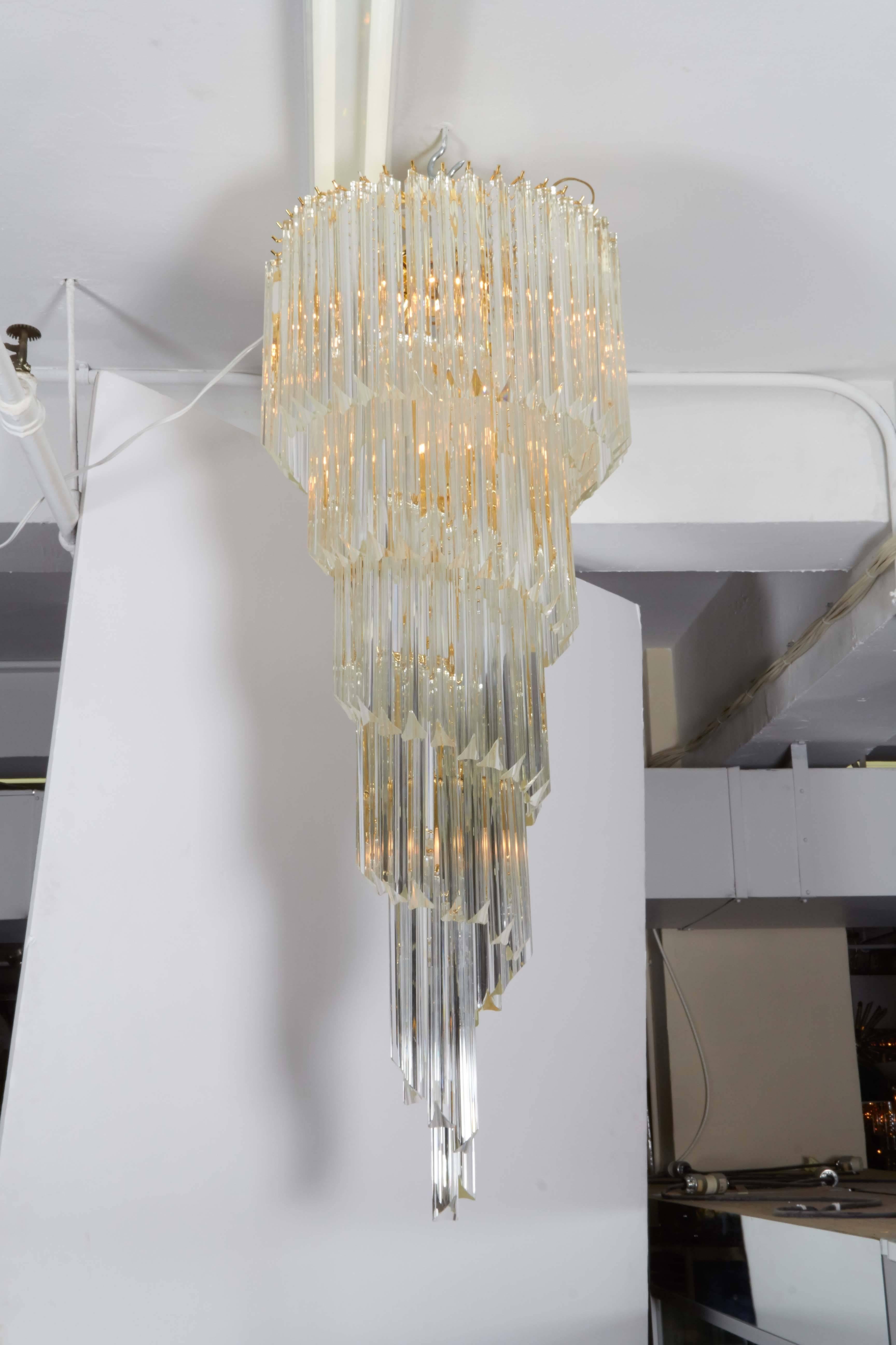 An impressive large scale chandelier, surrounded triedri crystal prisms, spiraling down from a four tier frame in brass. This fixture remains in very good condition, minor wear to metal and minuscule chips to prisms consistent with age and
