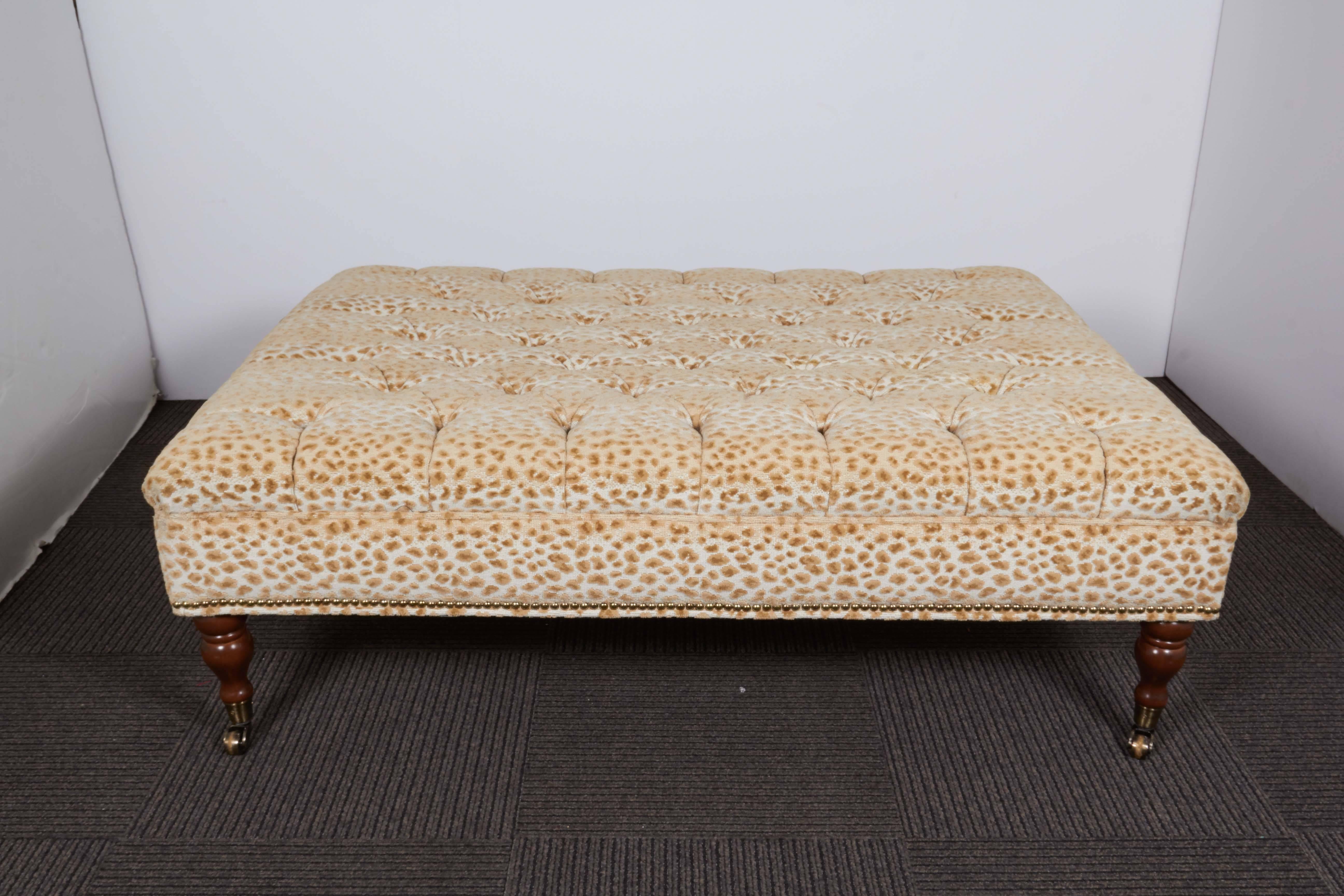 An oversized ottoman, following the style of George Smith, with tufted cushion seat with animal spot print, with brass nailhead trim, on turned wood, baluster form legs with caster wheels. Very good condition, consistent with age and use.