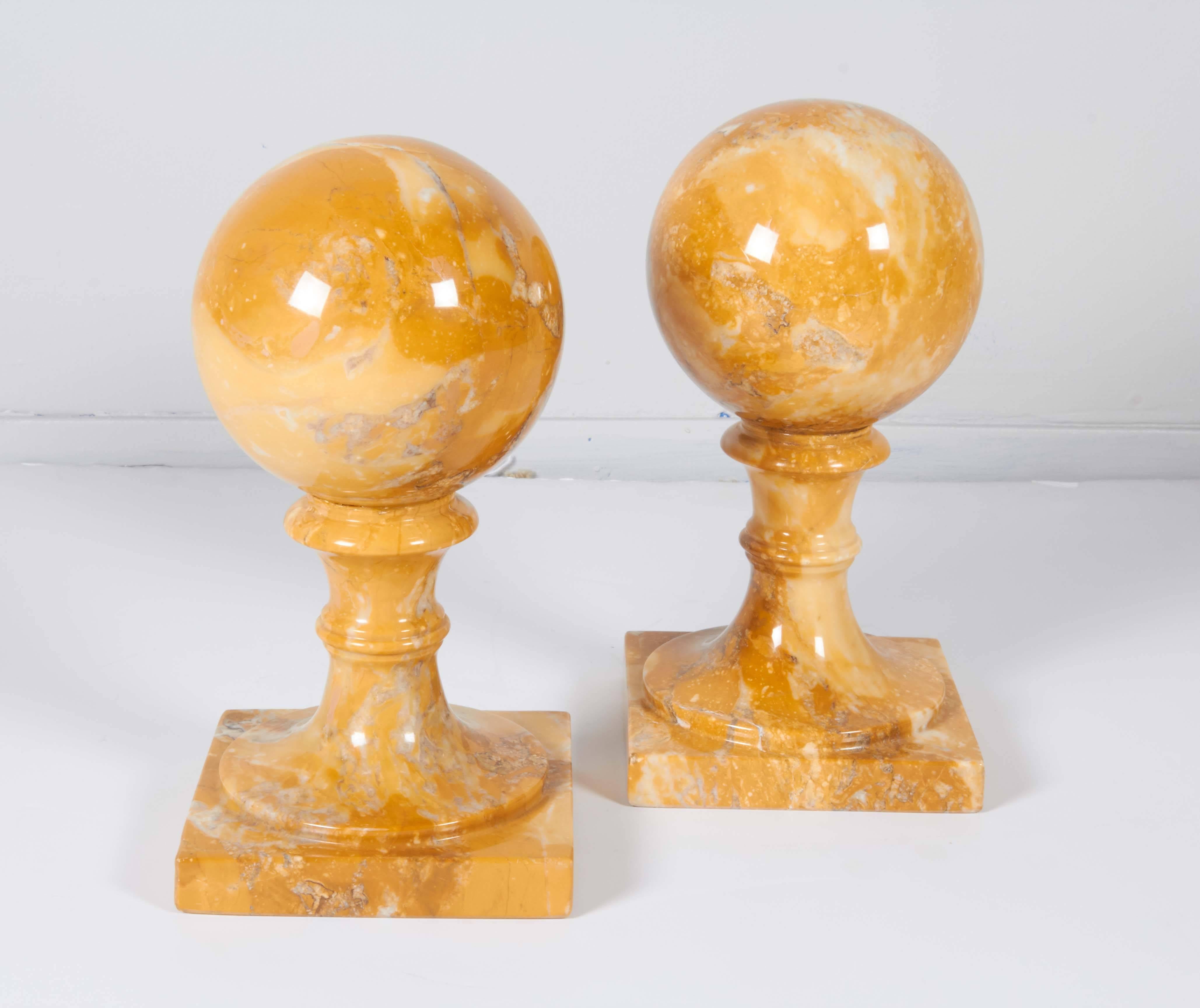 A pair of bookends with spheres mounted on classically styled pedestals, entirely crafted of carved and polished yellow marble; felt tabs to base. Very good condition, consistent with age and use.