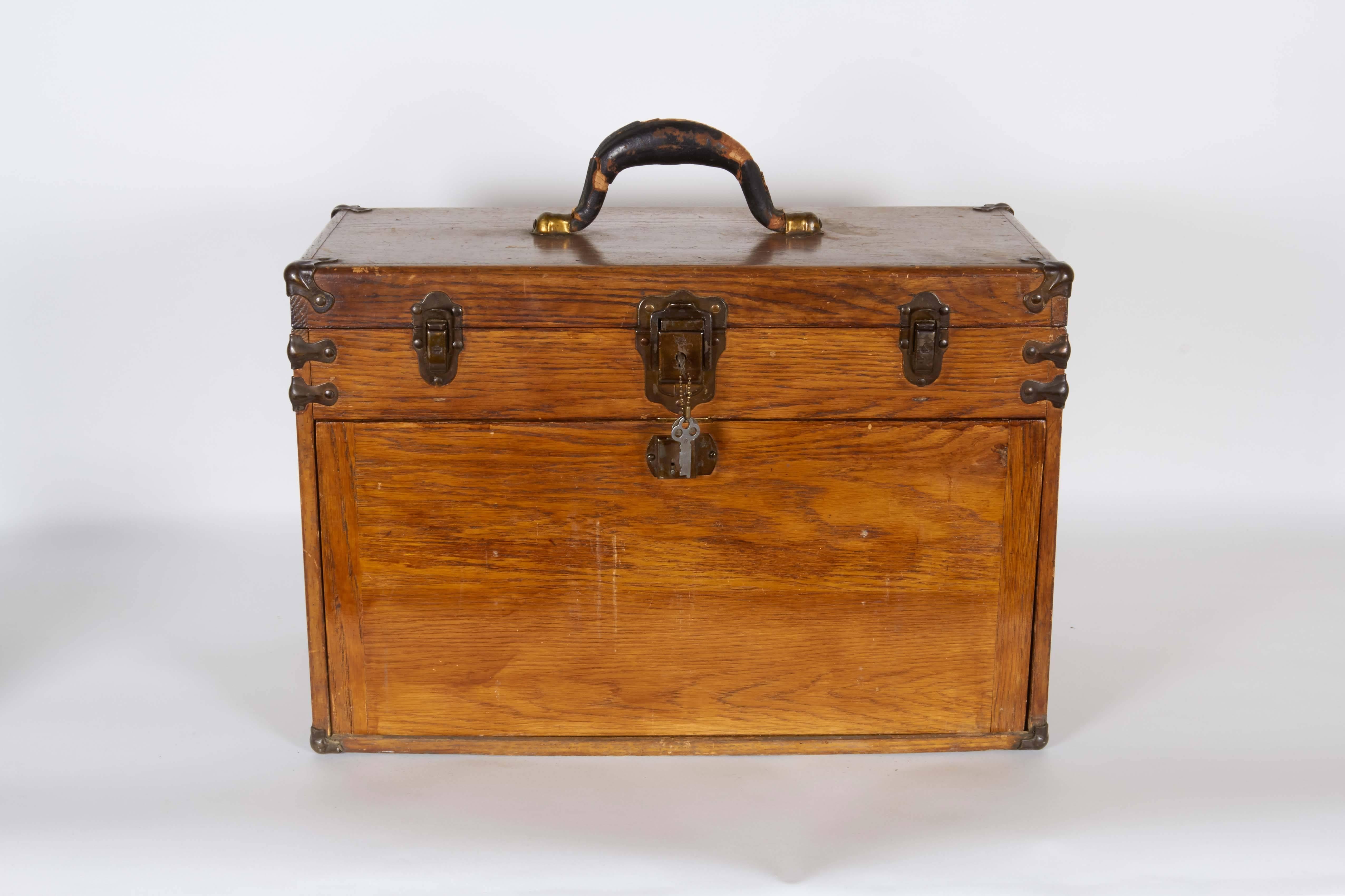 An oakwood toolbox, produced circa 1920s-1930s, with leather handle on hinged lid, interior lined with green felt and the original mirror. Below, a locking panel, which may slide in and out from the base, reveals seven drawers of varying sizes. This