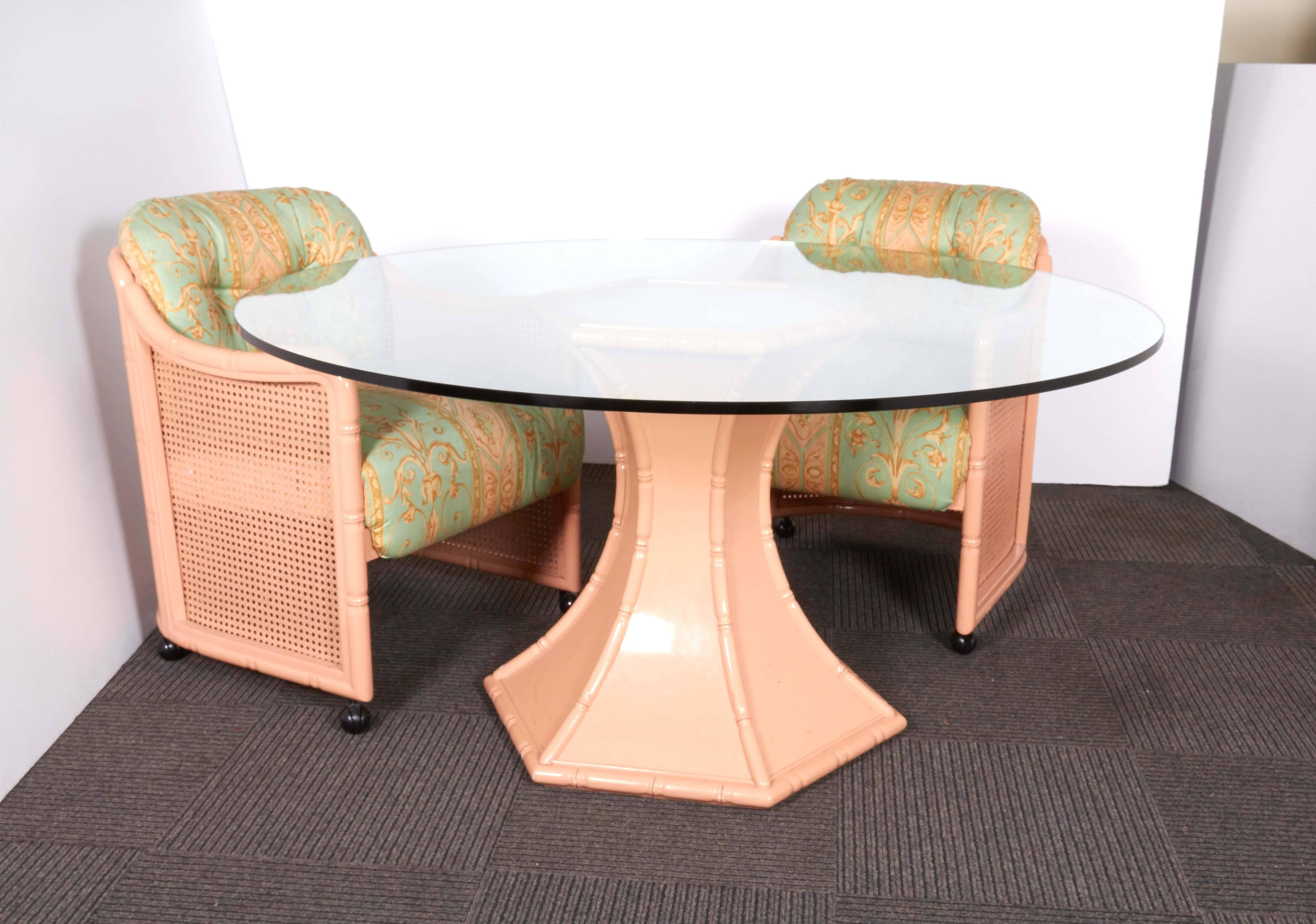 This dining set by Giorgetti, produced circa 1970s-1980s, evoking the Hollywood Regency style, includes a pink table base with round glass top, and eight matching tub chairs, each with caned sides, cushioned seat and back on caster wheels, the