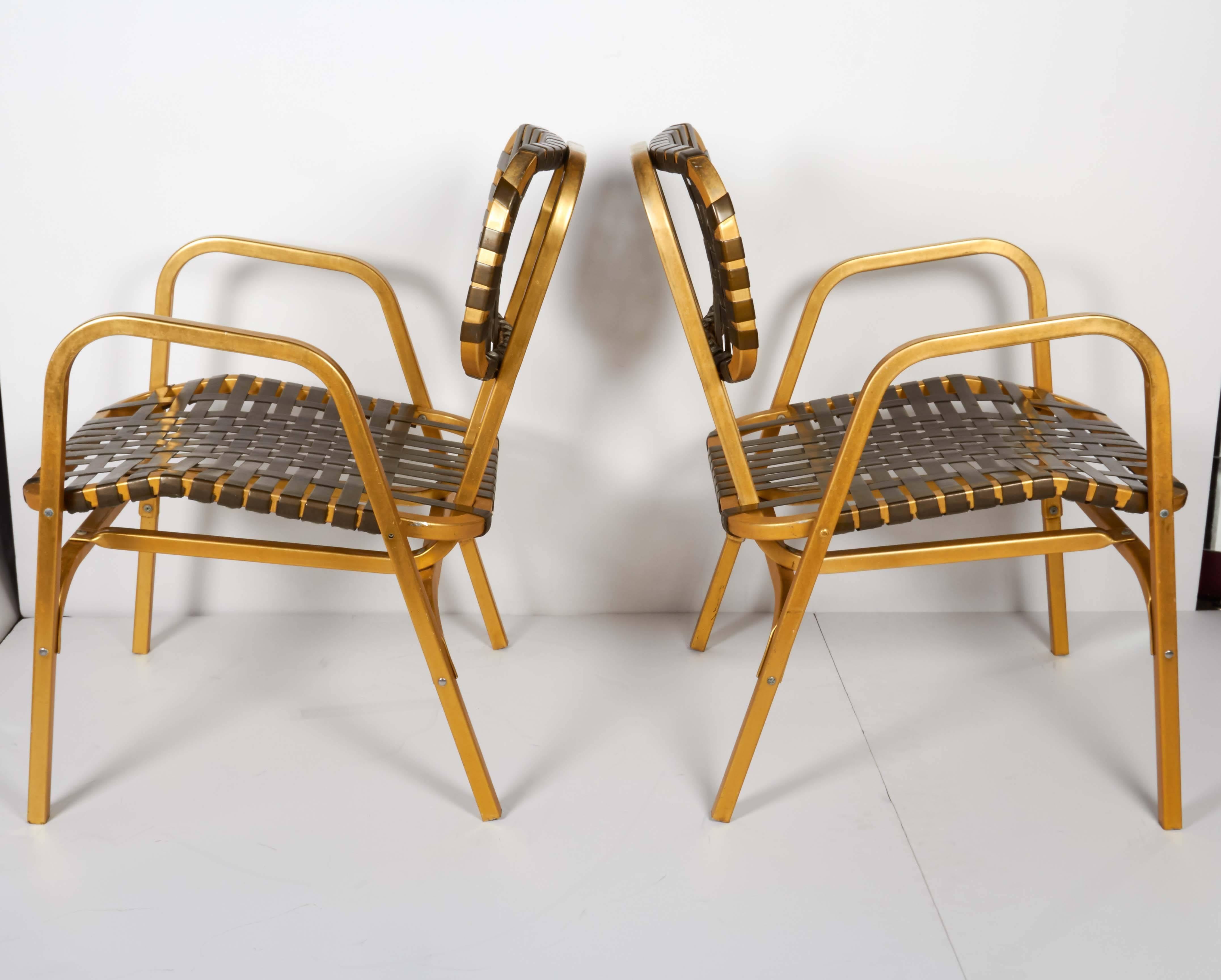 Joyful pair of lawn armchairs with lightweight aluminum frames with brass coated finish. Highly stylized design with uber chic Mid-Century modernist silhouettes. Chairs feature original woven vinyl bands in deep brown hues across the backs and