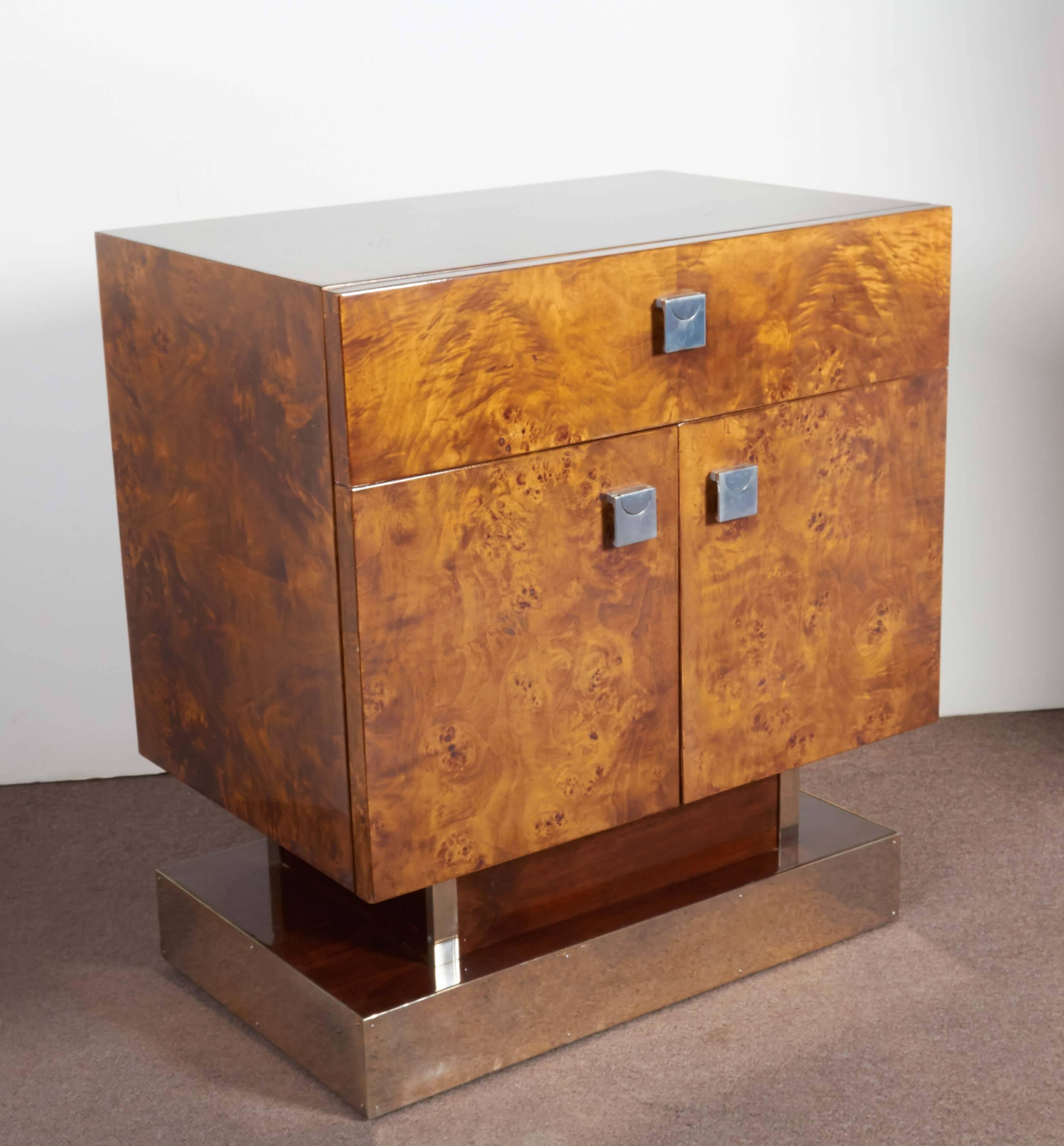 Pair of Art Deco style cubist nightstands or side tables.
Exotic burlwood on top, front and sides with large single drawer above two doors bearing geometric design nickeled mounts. The whole set on a two step square pedestal base with nickeled
