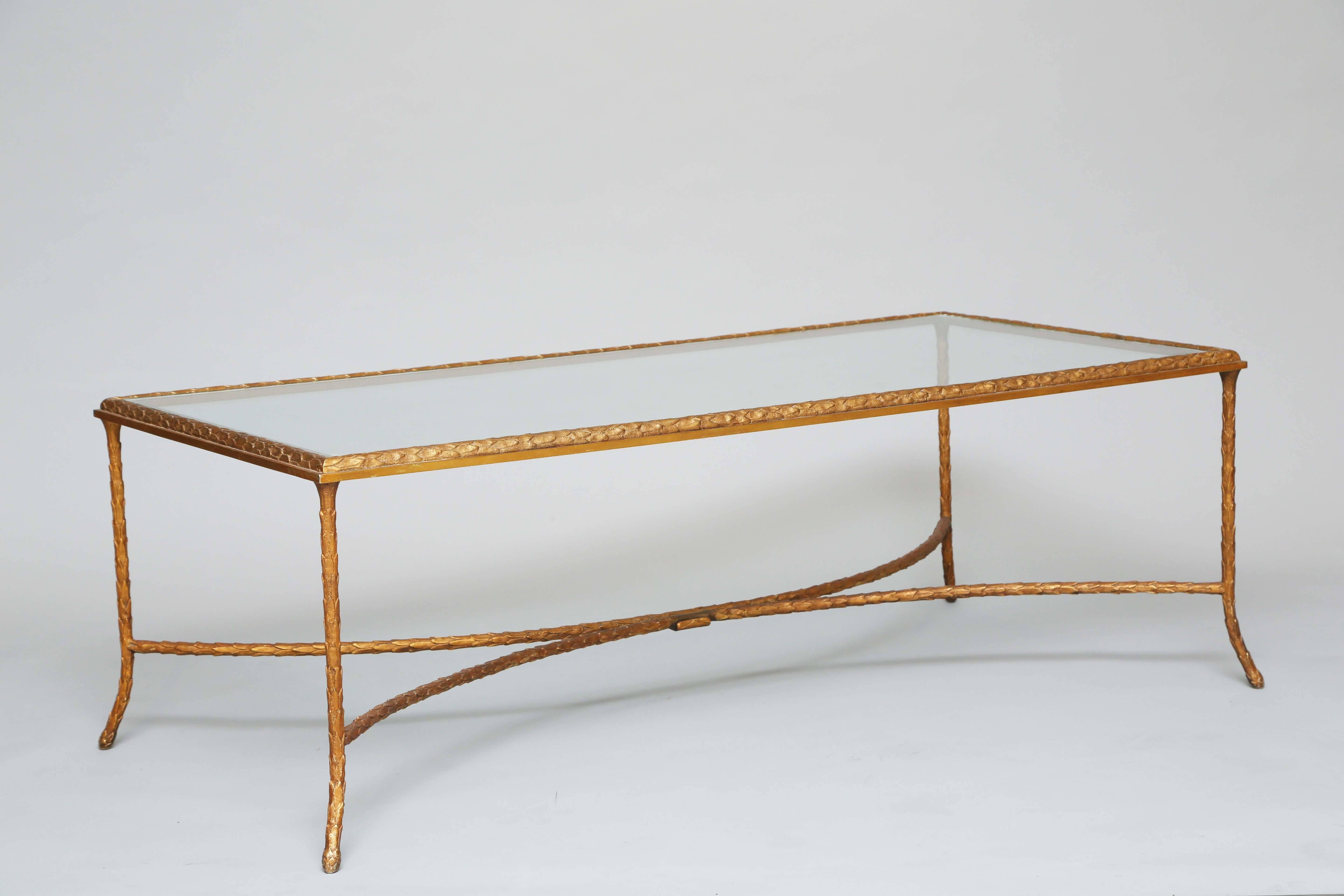 Coffee table of gilded bronze in the style of Baguès, having a rectangular top of glass on a table base of gilded bronze its foliate frame on splayed legs, with double arched stretcher.