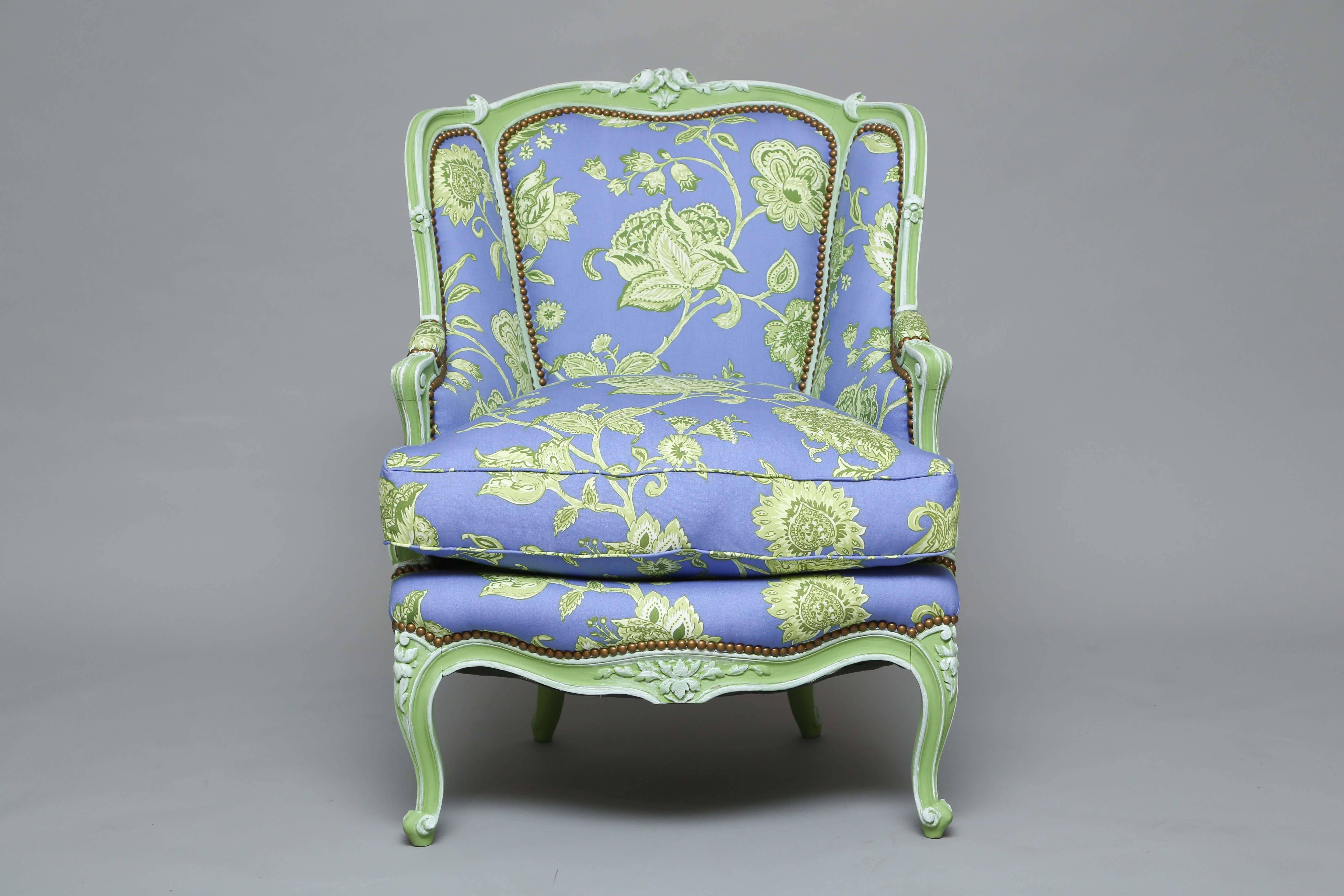 Pair of upholstered bergere armchairs, in the Louis XV style, each having a painted finish, with a shaped and domed padded back surmounted by a floral crest, joined to the cushioned seat by out scrolled acanthine-carved arms, the shaped