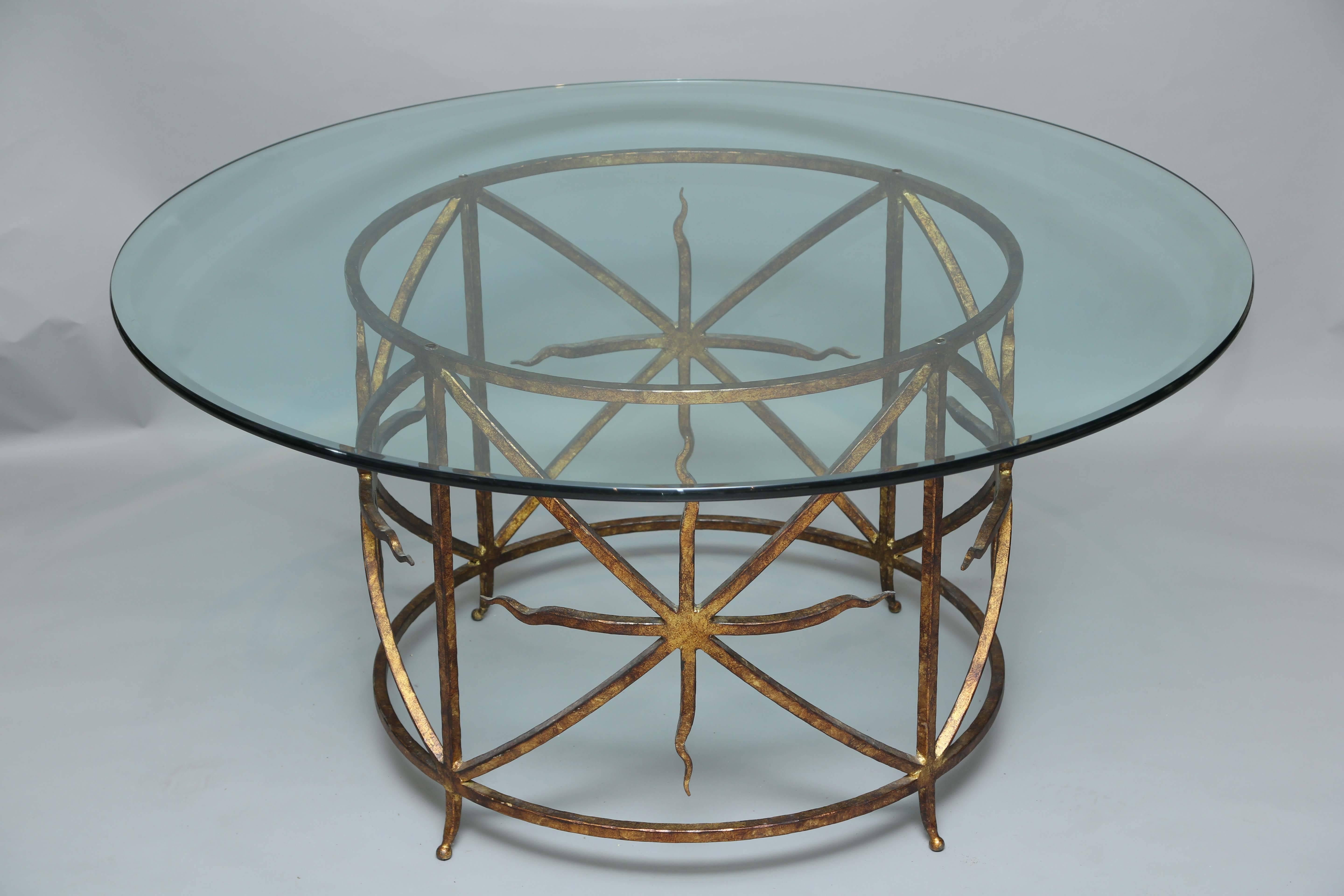 Center or dining table, having a round top of glass on circular base of gilded iron, divided into four sections, with bowed X-supports, centered with 