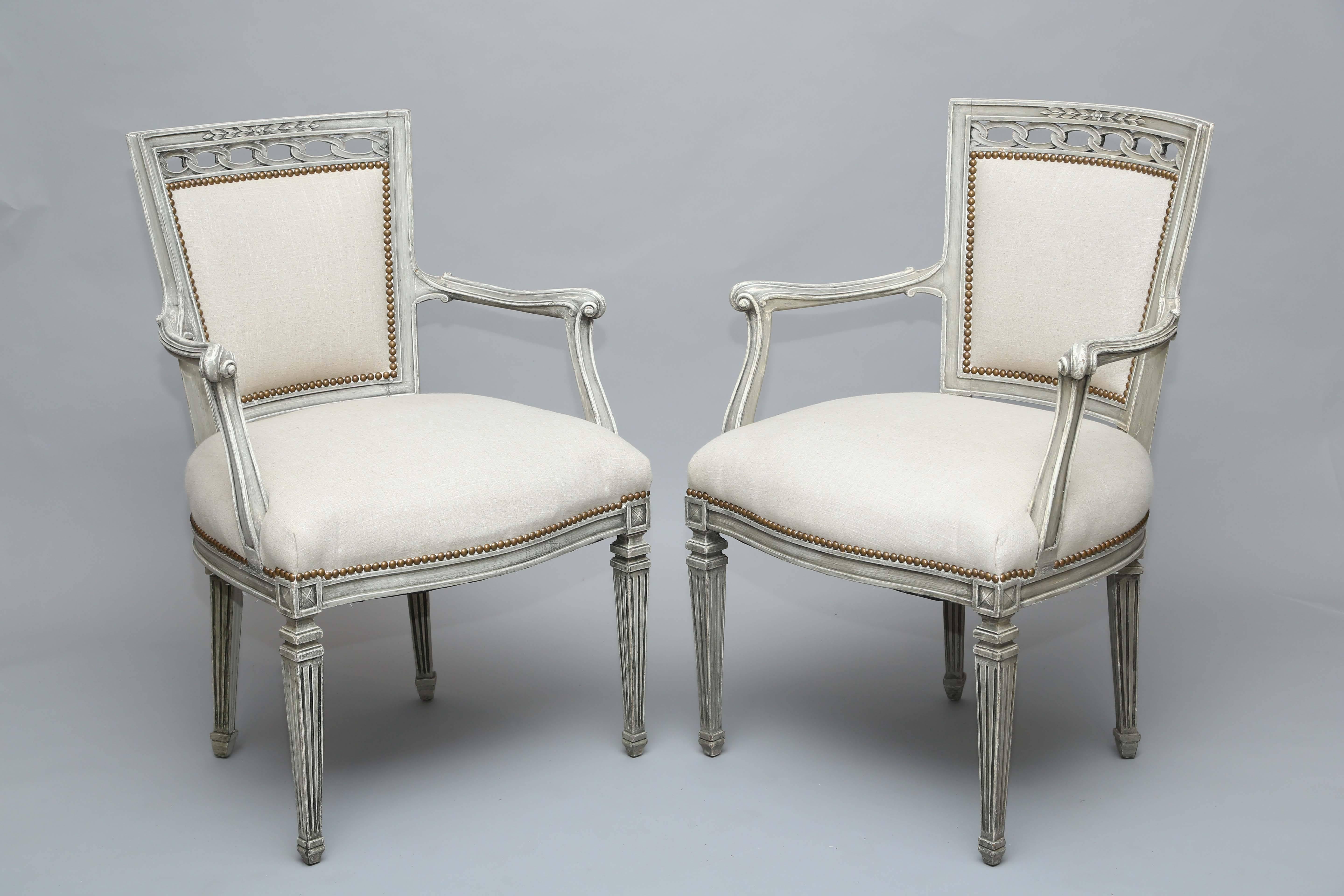 Pair of armchairs, having a painted finish showing natural wear, its bowed channelled crestrail inset with carved leaf decoration, over pierced, interlocking rings, a padded tapering back, into stuff-over seat, its arms ending in scrolls, raised on