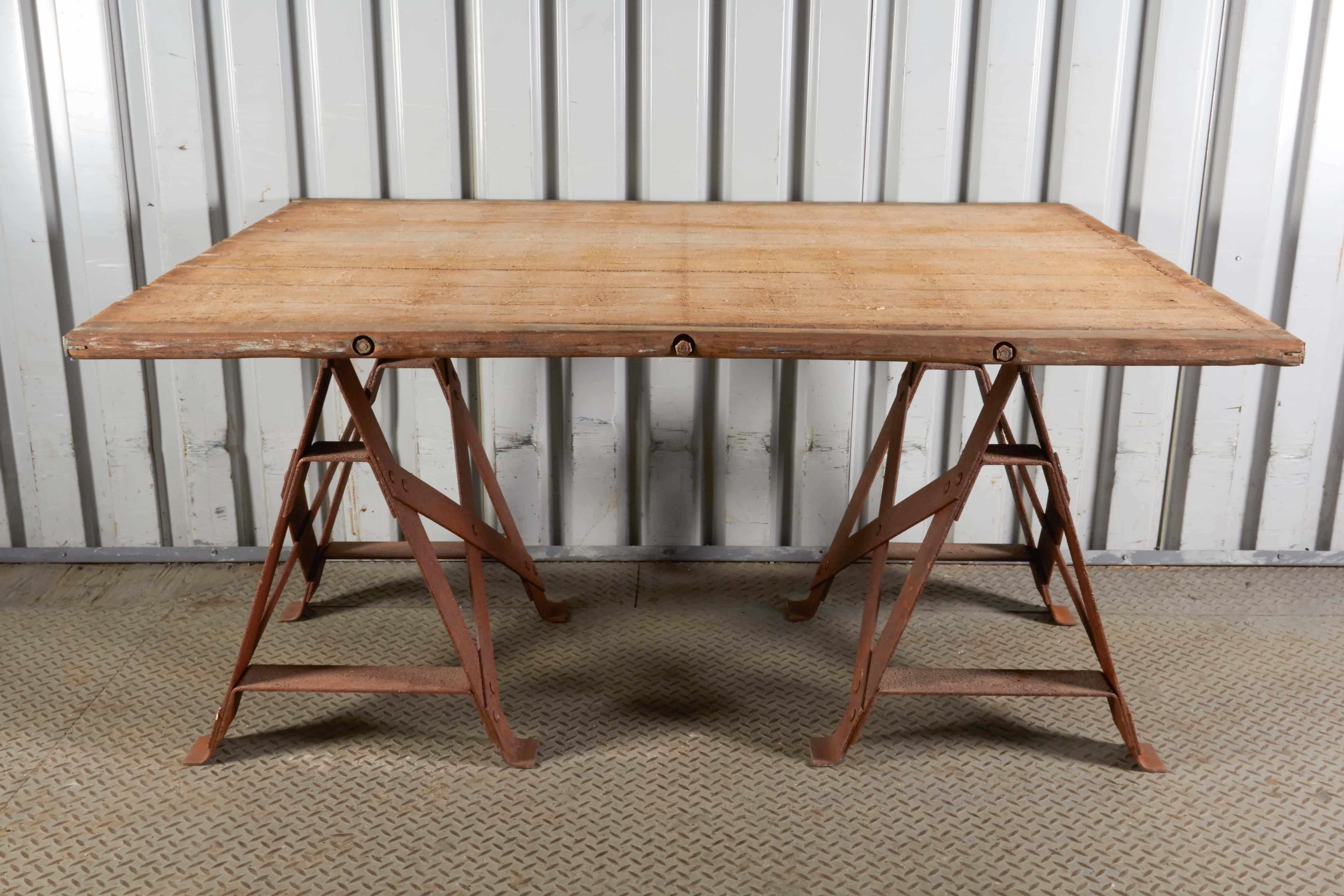 Industrial style trestle table consisting of rustic rough-hewn wood top and riveted iron bases.