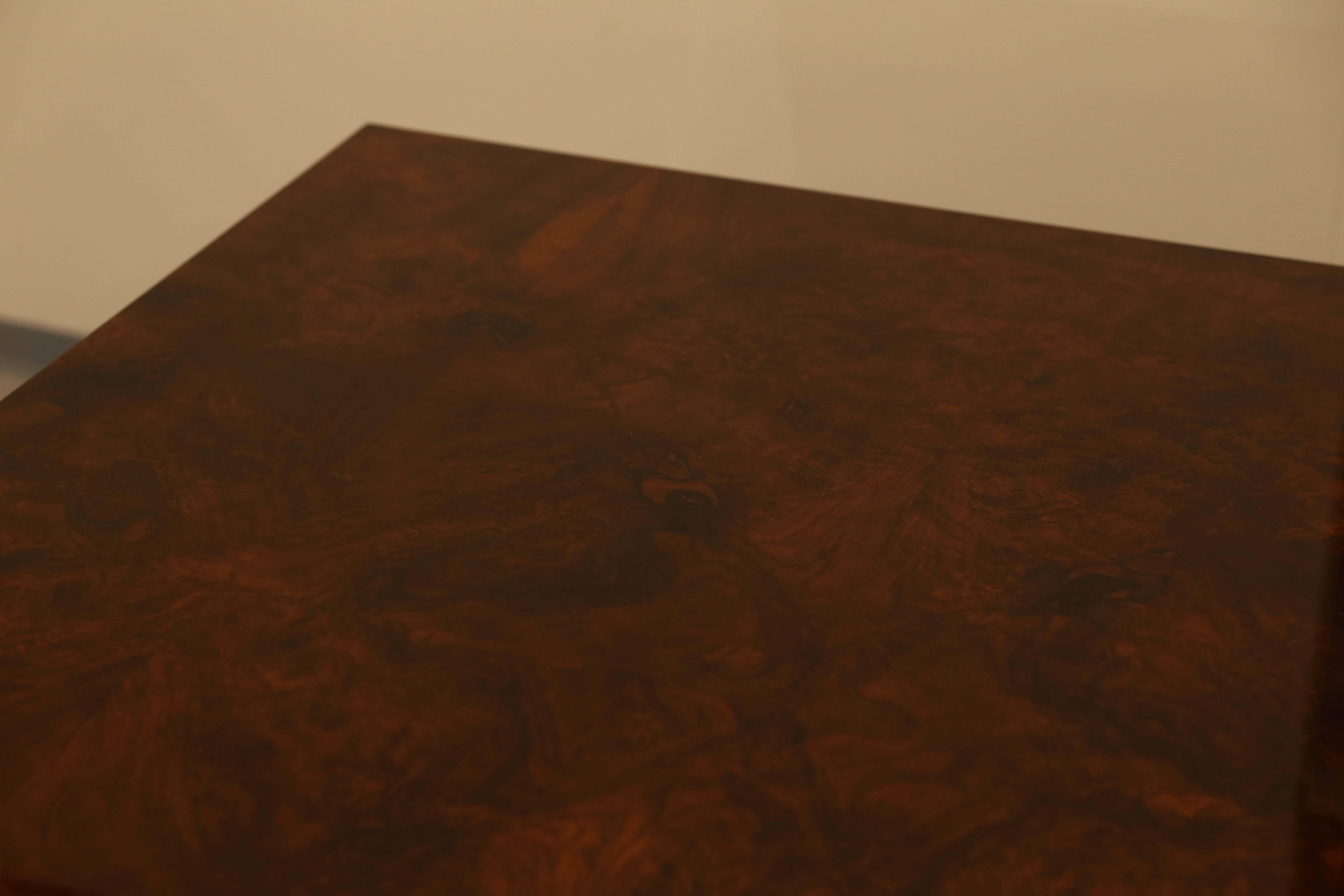 The wide tabletop is displaying a beauty of burl walnut. It supported by two semi-circular legs that are connected to the wide rectangular base. The base is decorated with chrome elements on the tips of the base. The table has two side extensions