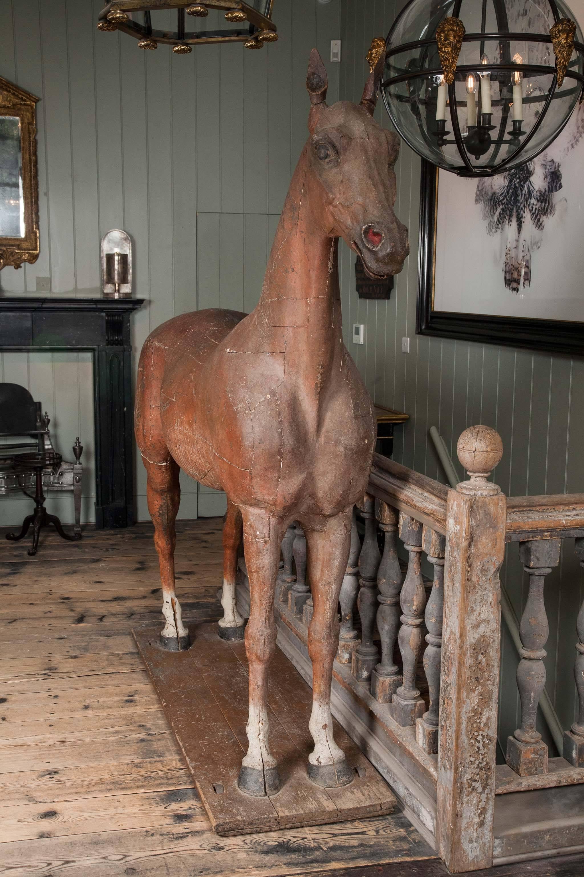 A late 18th-early 19th century full size wooden sculpture of a horse, with tail made from horse hair, resting on a rectangular wooden base mounted on four castors.