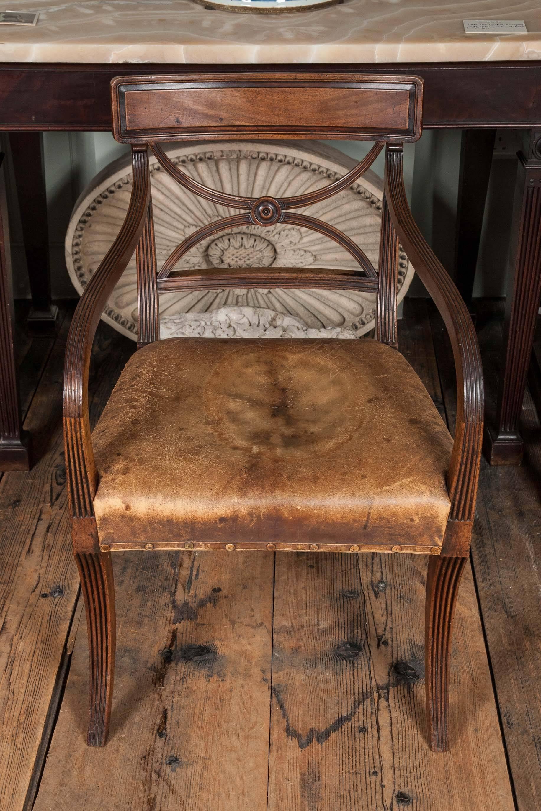 A set of 14 late George III mahogany dining chairs of Sheraton
design with panelled tablet-shaped cresting rails, over curved bar backs and centred by turned roundels, with green leather seats, on reeded sabre legs.