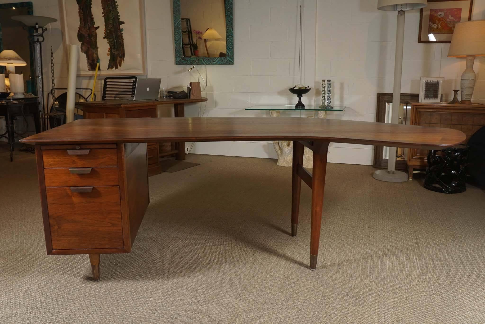 Here is a great Modern desk in walnut with a large boomerang top.
The desk has three drawers including a built in file drawer. There is also a pull-out tray. The top has a surround marquetry border.