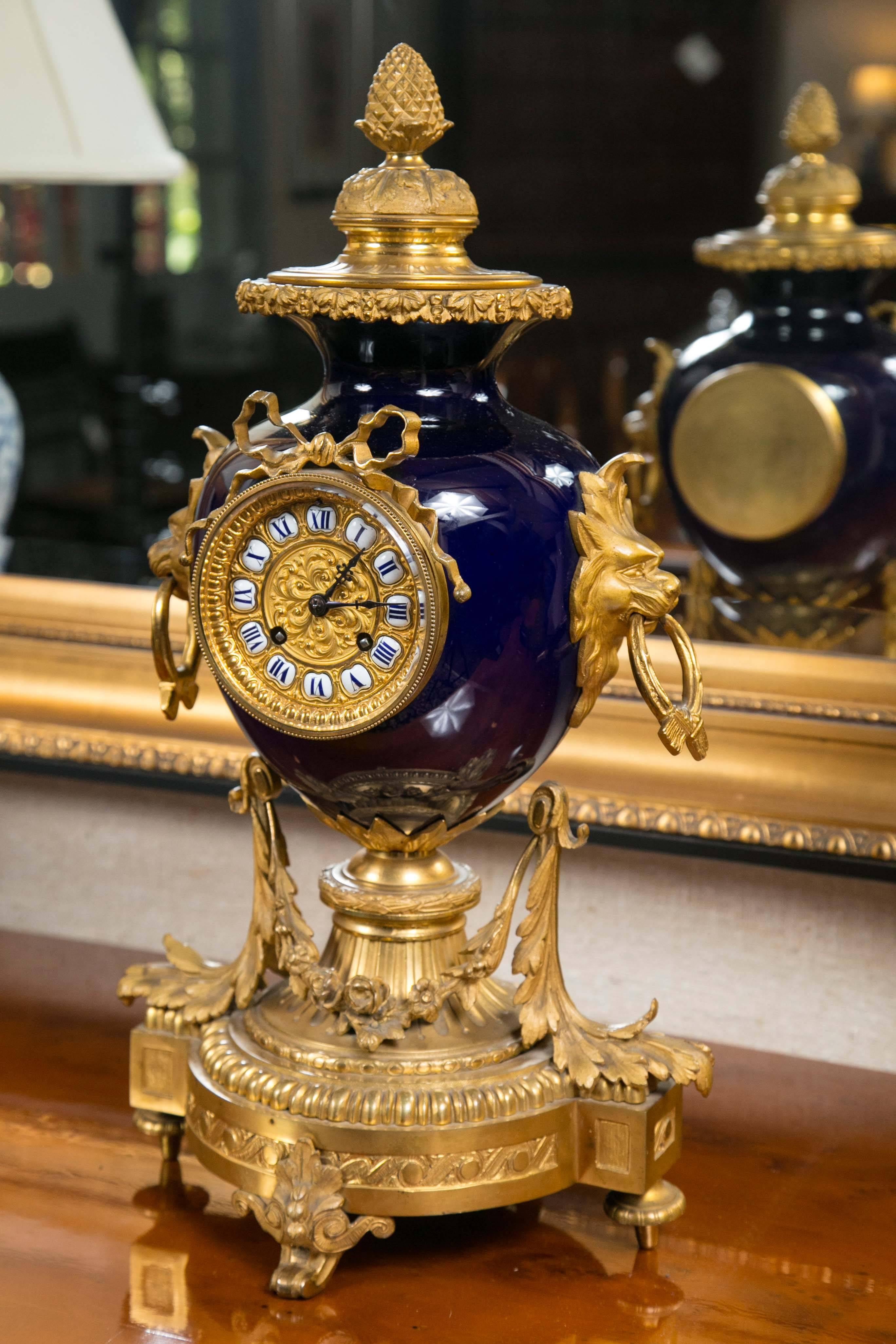 Elegant French ormolu mantel clock with stunning cobalt blue vase with lion head handles with crossed sash rings. Clock features intricate gilt face with individual enamel numbers and bow appliqué. Base is comprised of a fluted column with delicate