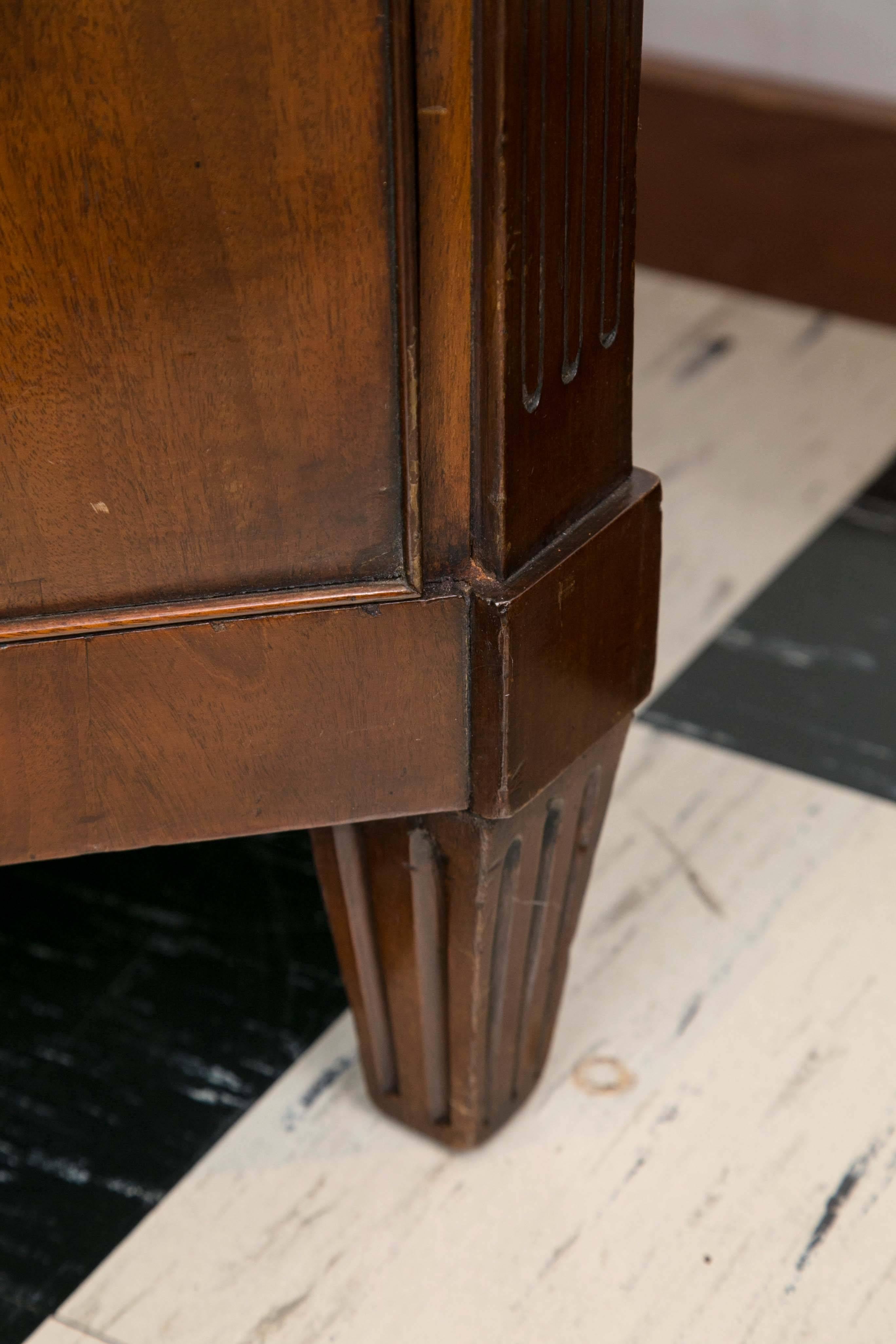 Unusual Dutch mahogany chest of drawers features chamfered fluted sides ending in fluted tapered feet framing a stepped apron. The figured mahogany shaped top rests over a dentil frieze above four graduated drawers with bookmatched veneers.