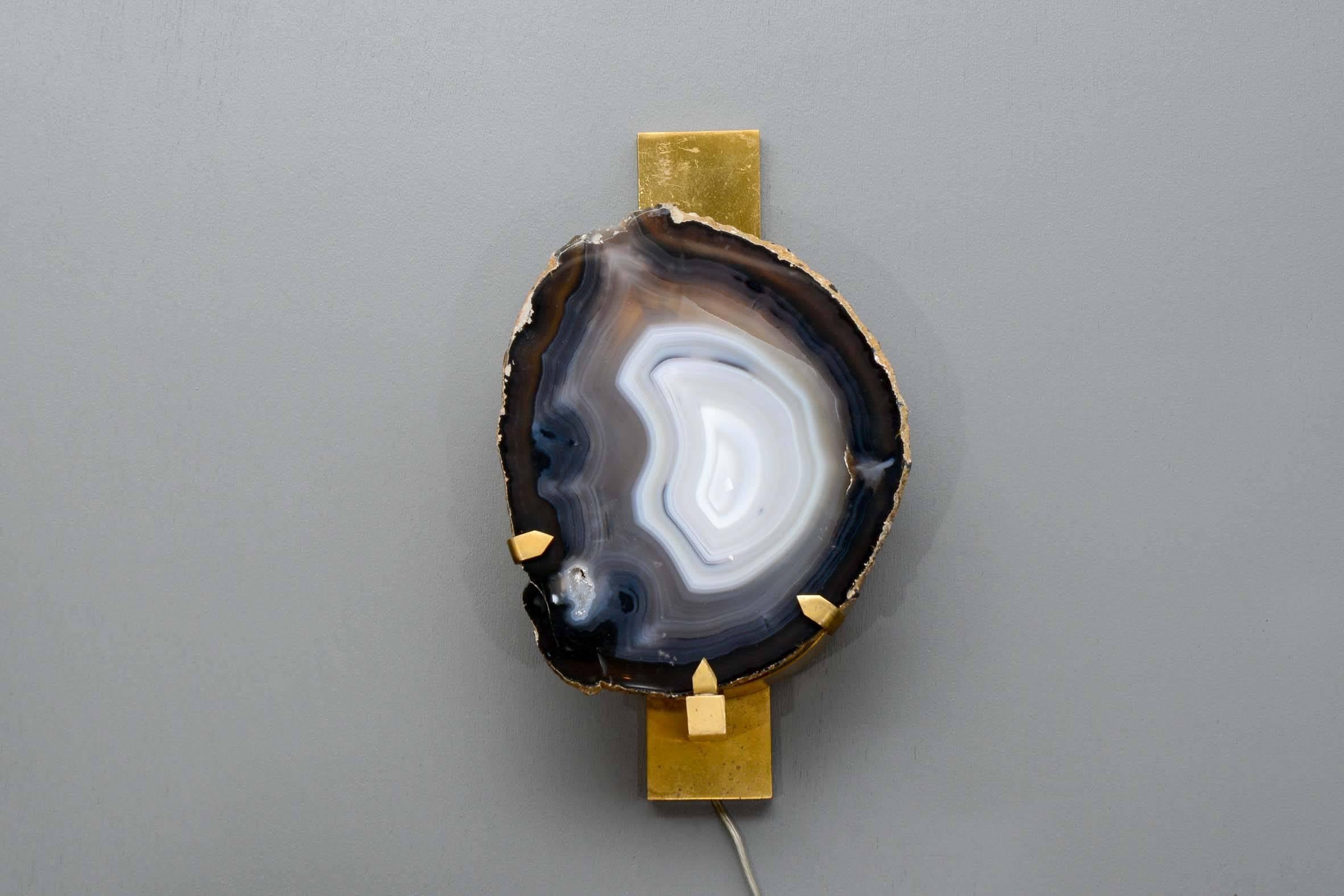 Small pair of wall sconces made of brass structure and two slices of agate stone hiding the bulb.